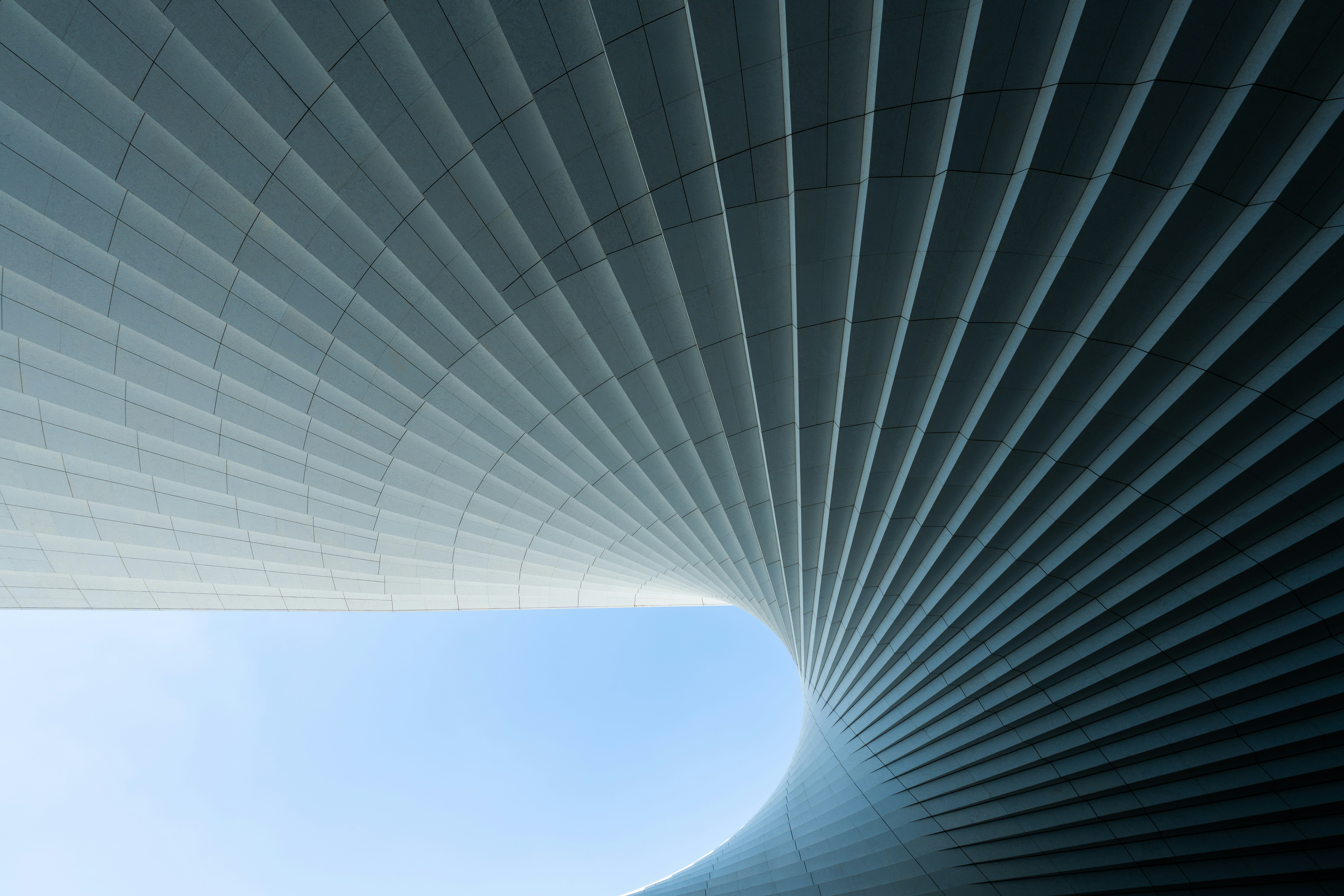 A curved architectural structure with repeating parallel lines against a clear blue sky