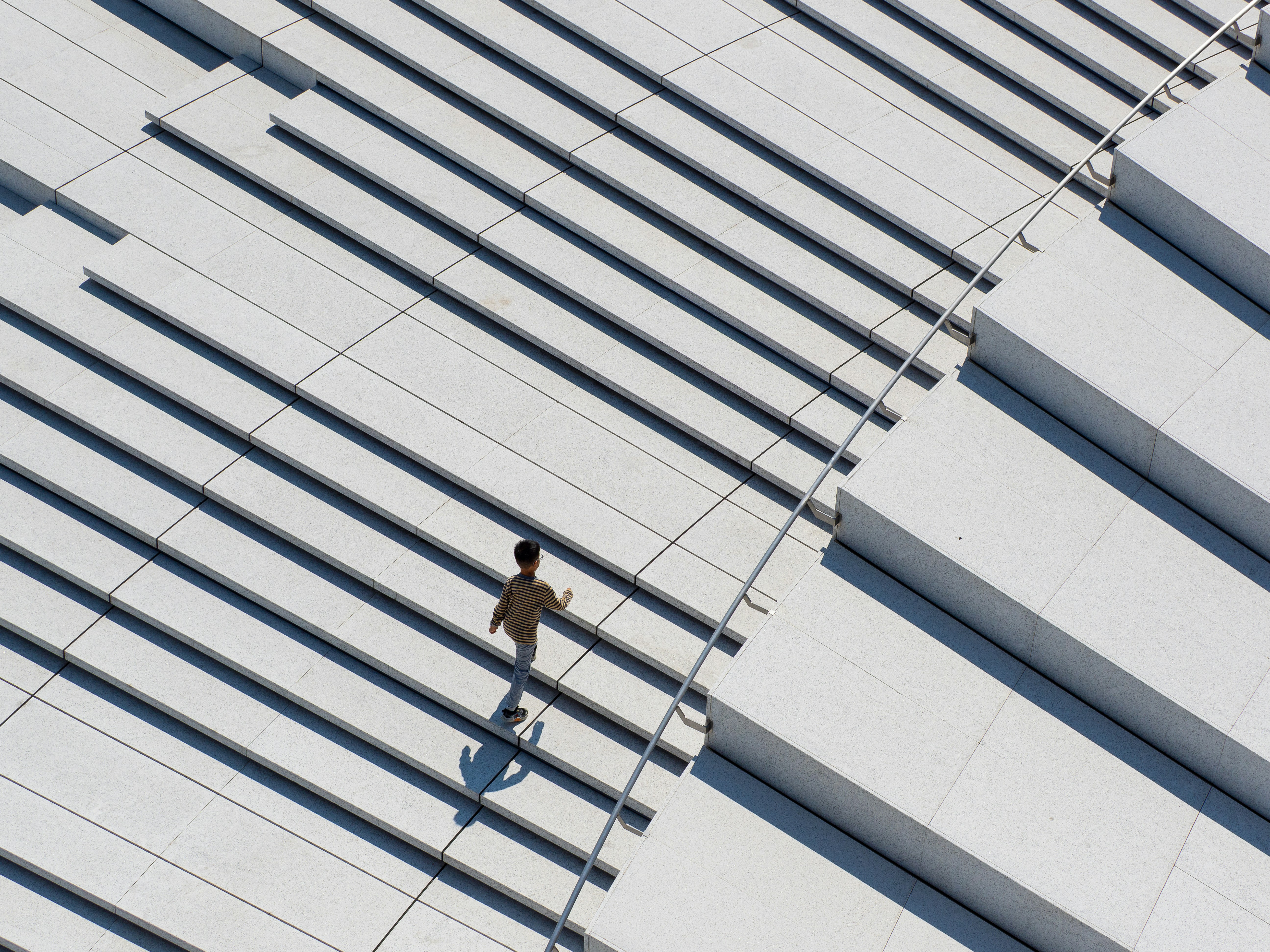 A person in a striped shirt walking up wide grey stone stairs