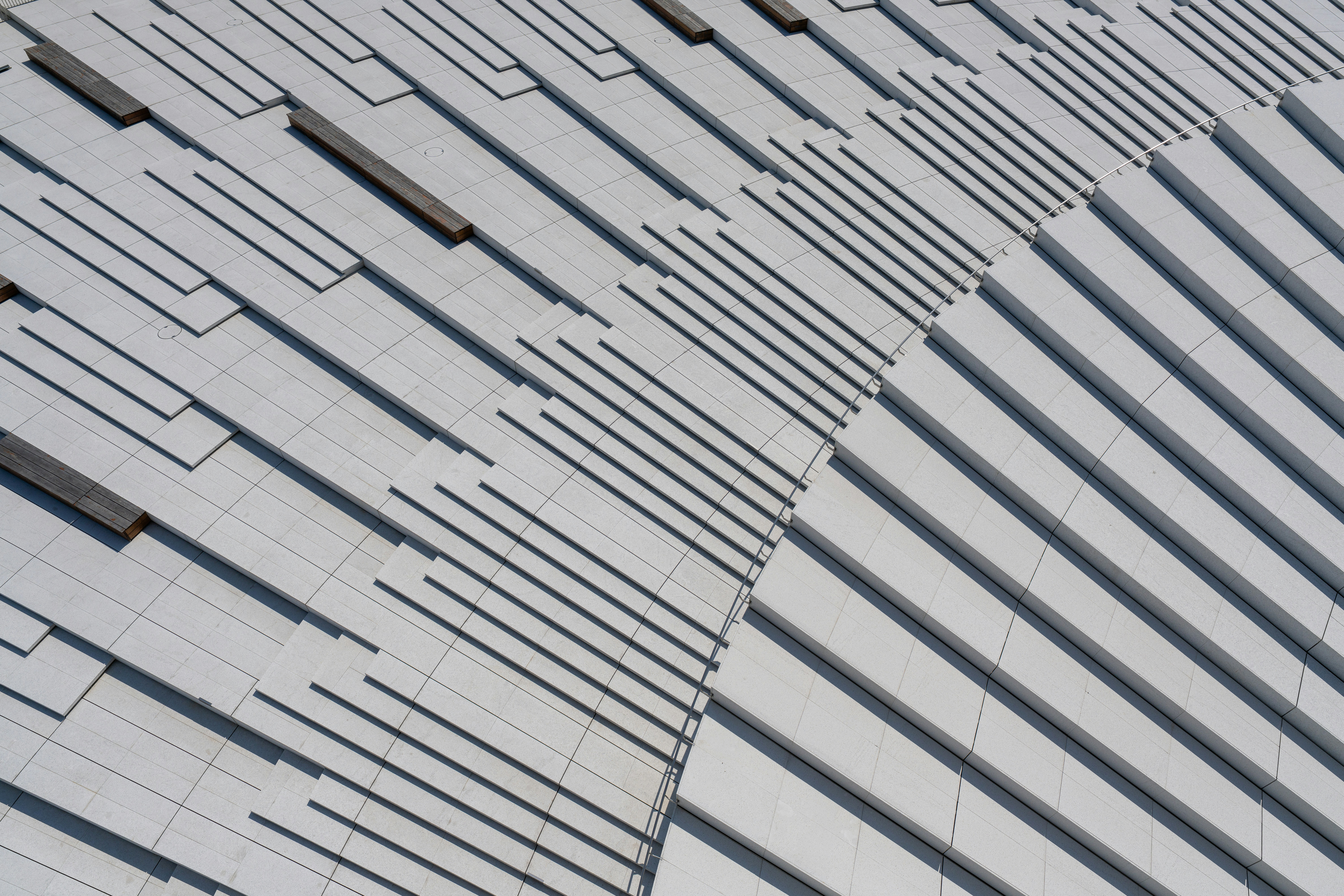 A geometric pattern of white stone steps and wooden benches from above