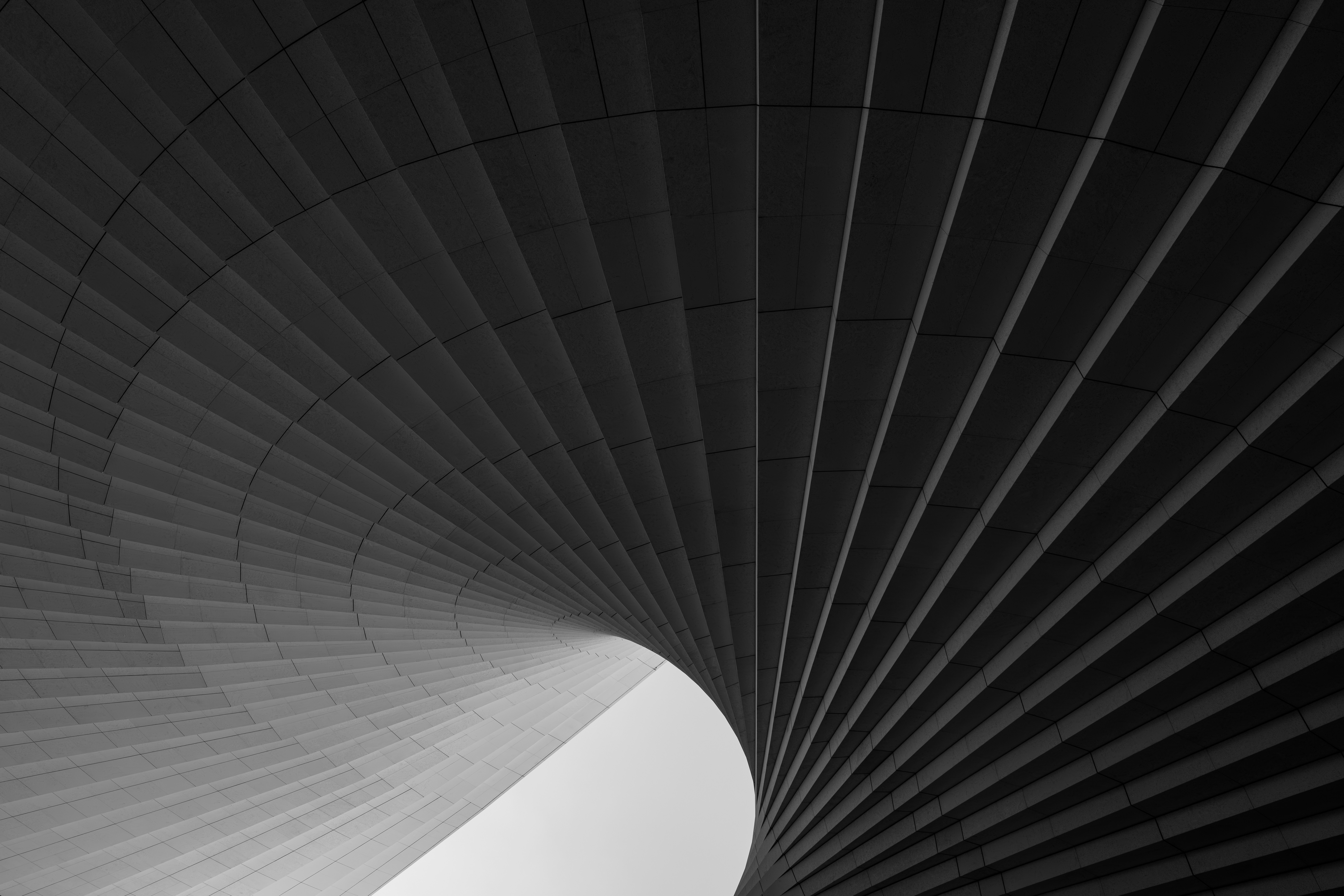 Curved architectural panels forming a spiraling tunnel with a bright light at the end