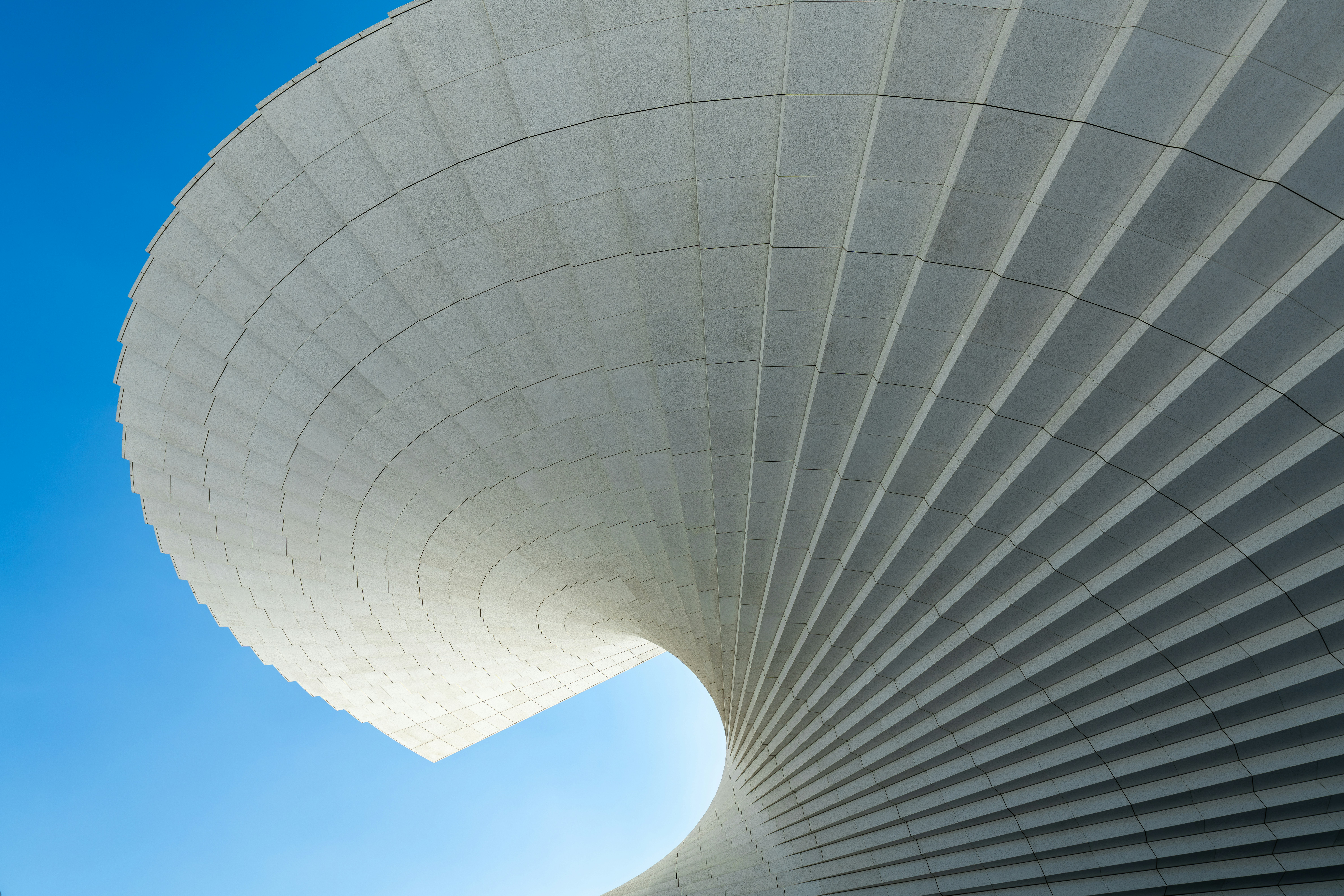A curved architectural structure with white tiled panels against a clear blue sky