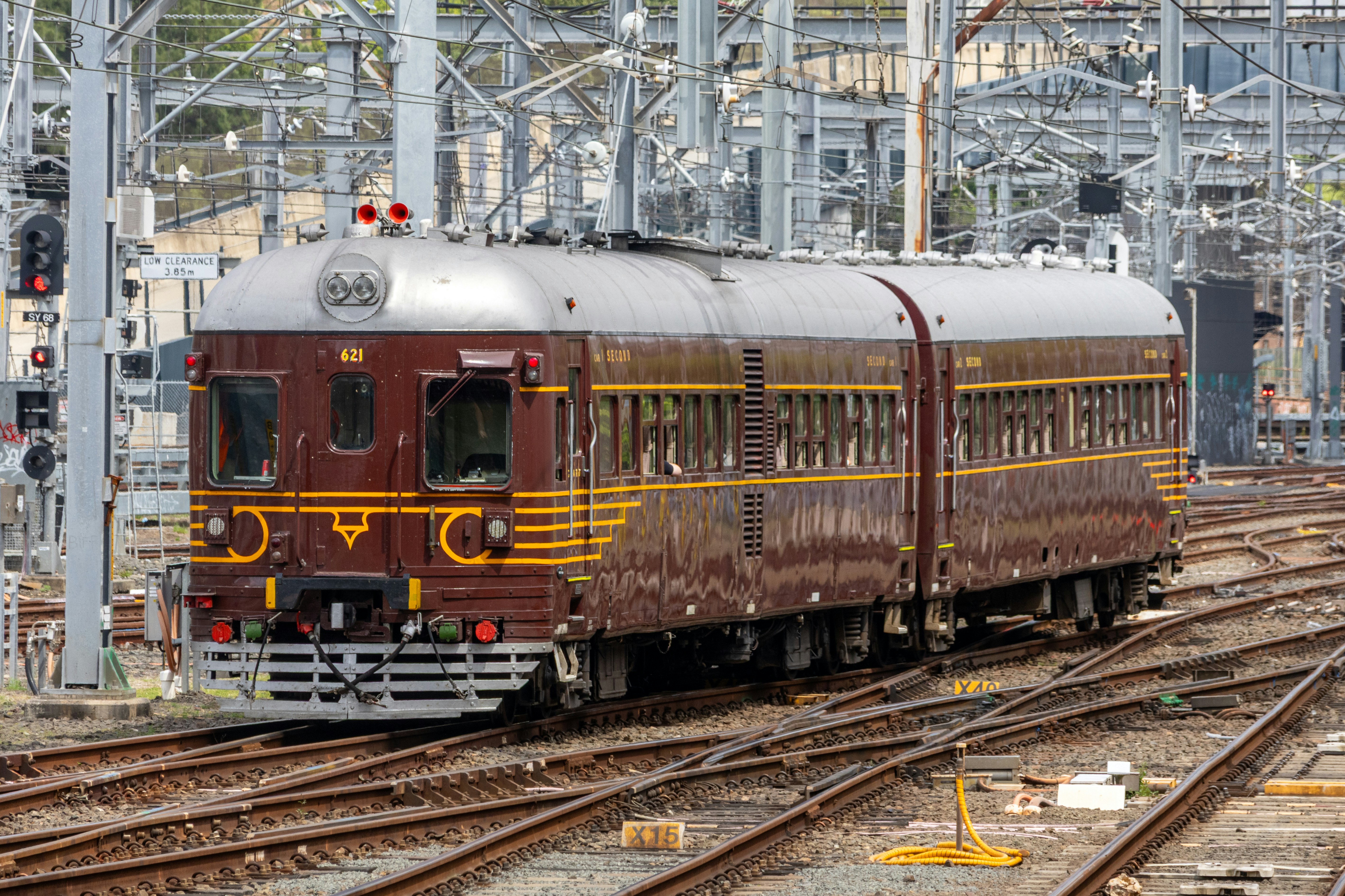 A vintage brown and silver passenger train on tracks at a rail yard