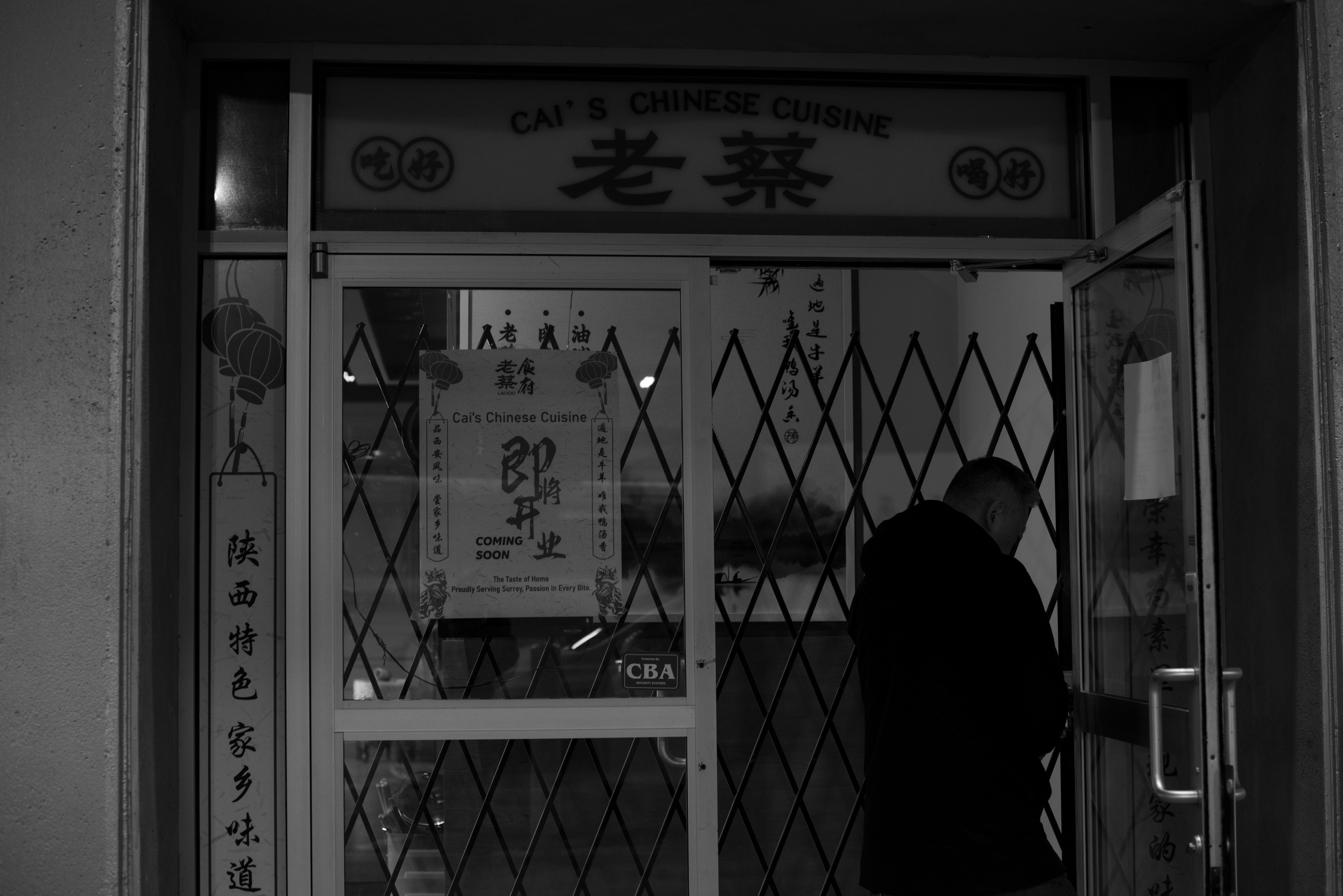 A person in a dark coat entering a restaurant with a sign reading Cai's Chinese Cuisine