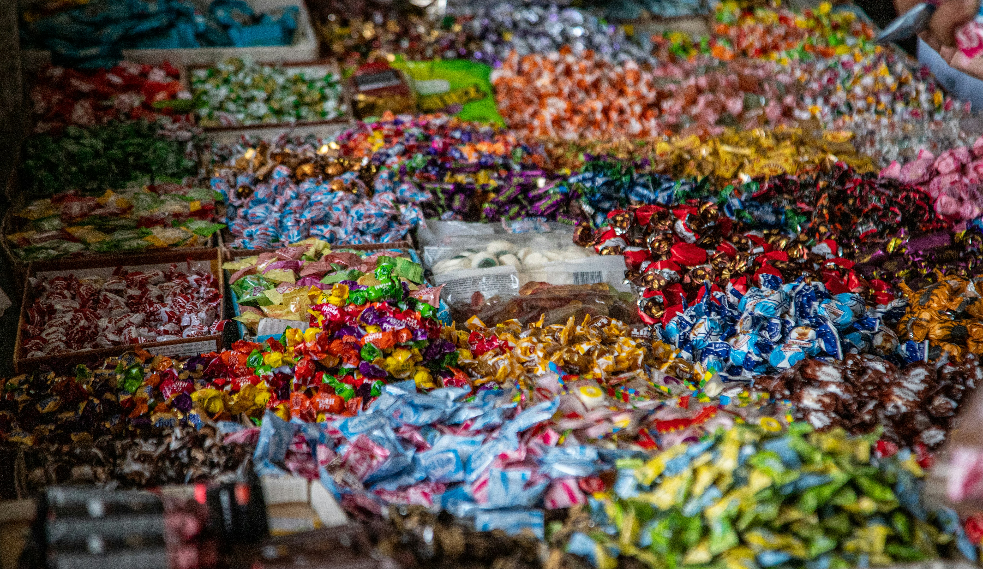 A large assortment of colorful wrapped candies displayed in bins at a market