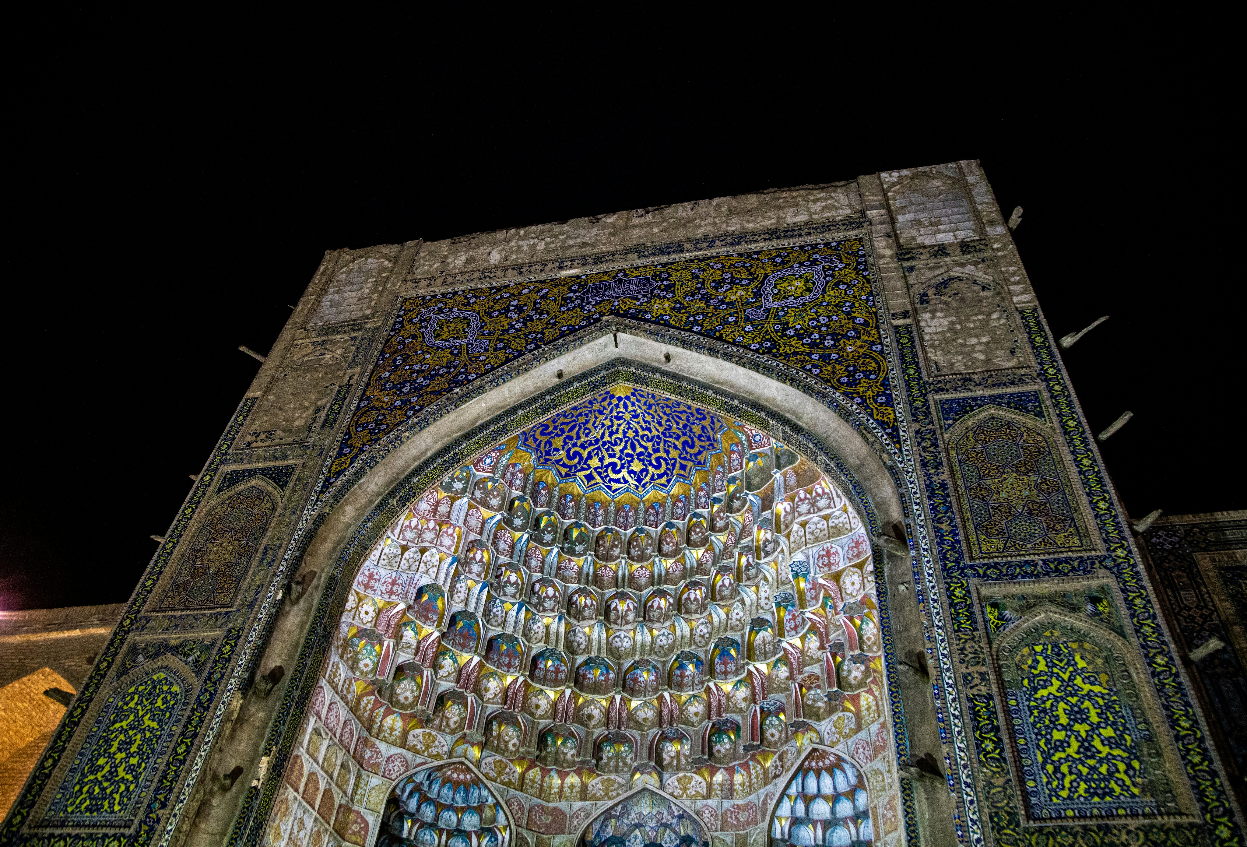 An ornate arched entrance with intricate blue and gold tilework at night