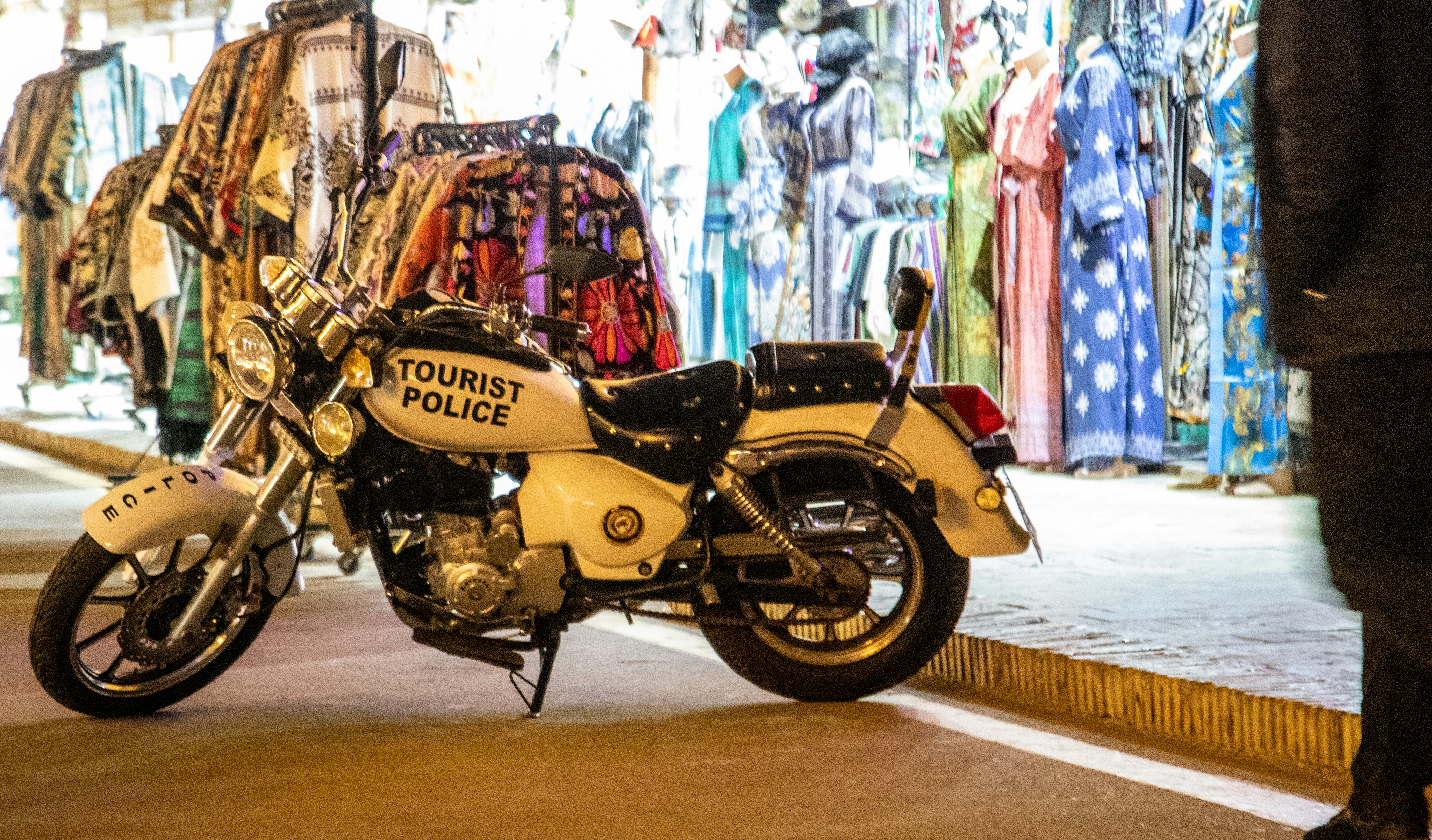 A white motorcycle labeled Tourist Police parked in front of a clothing market