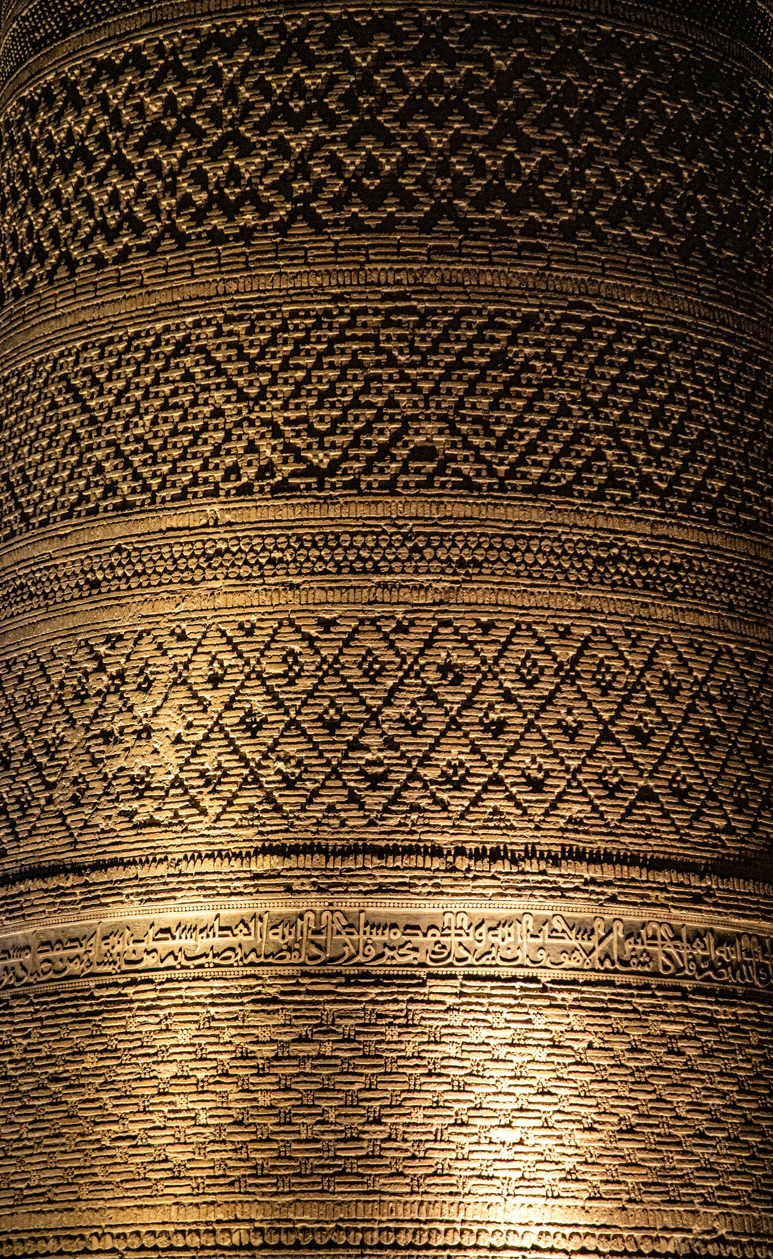 Intricate geometric brick patterns and Arabic calligraphy on a cylindrical tower wall