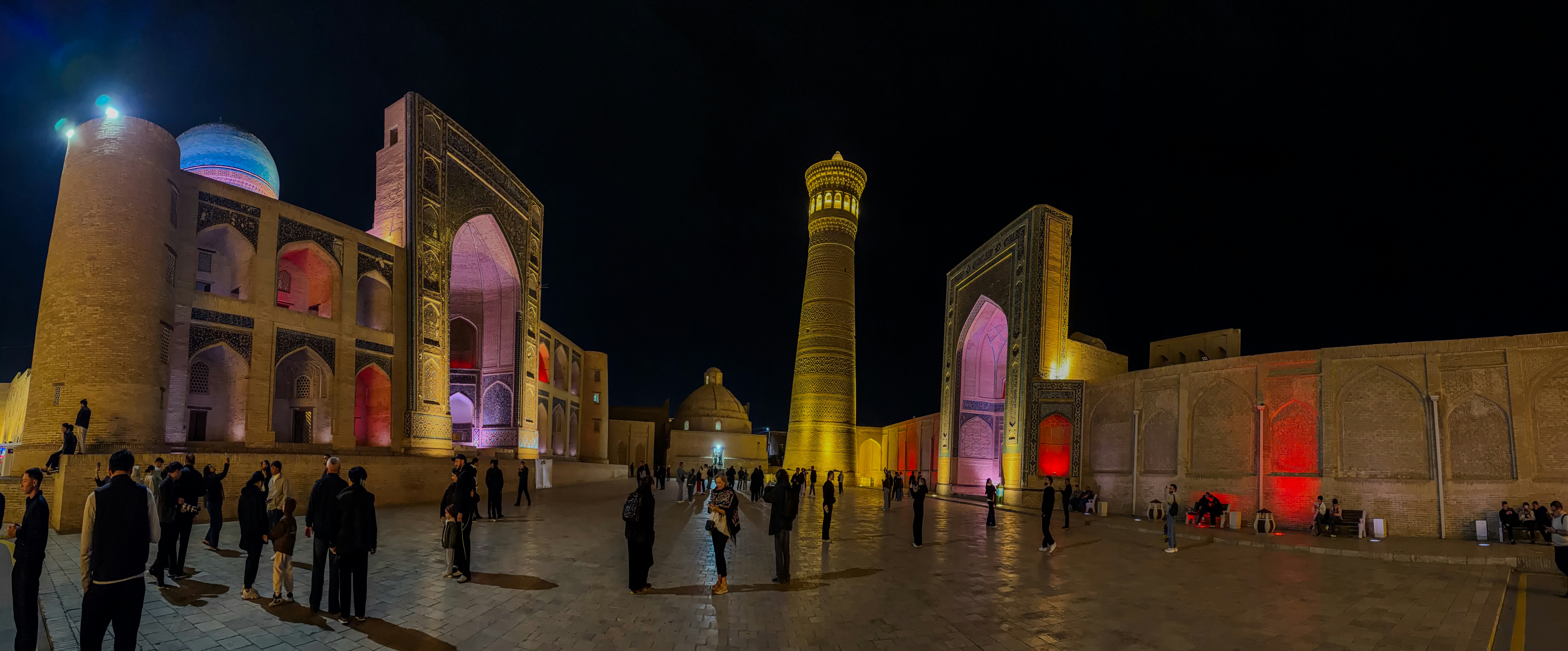 People walking in the Po-i-Kalyan complex in Bukhara at night with illuminated architecture