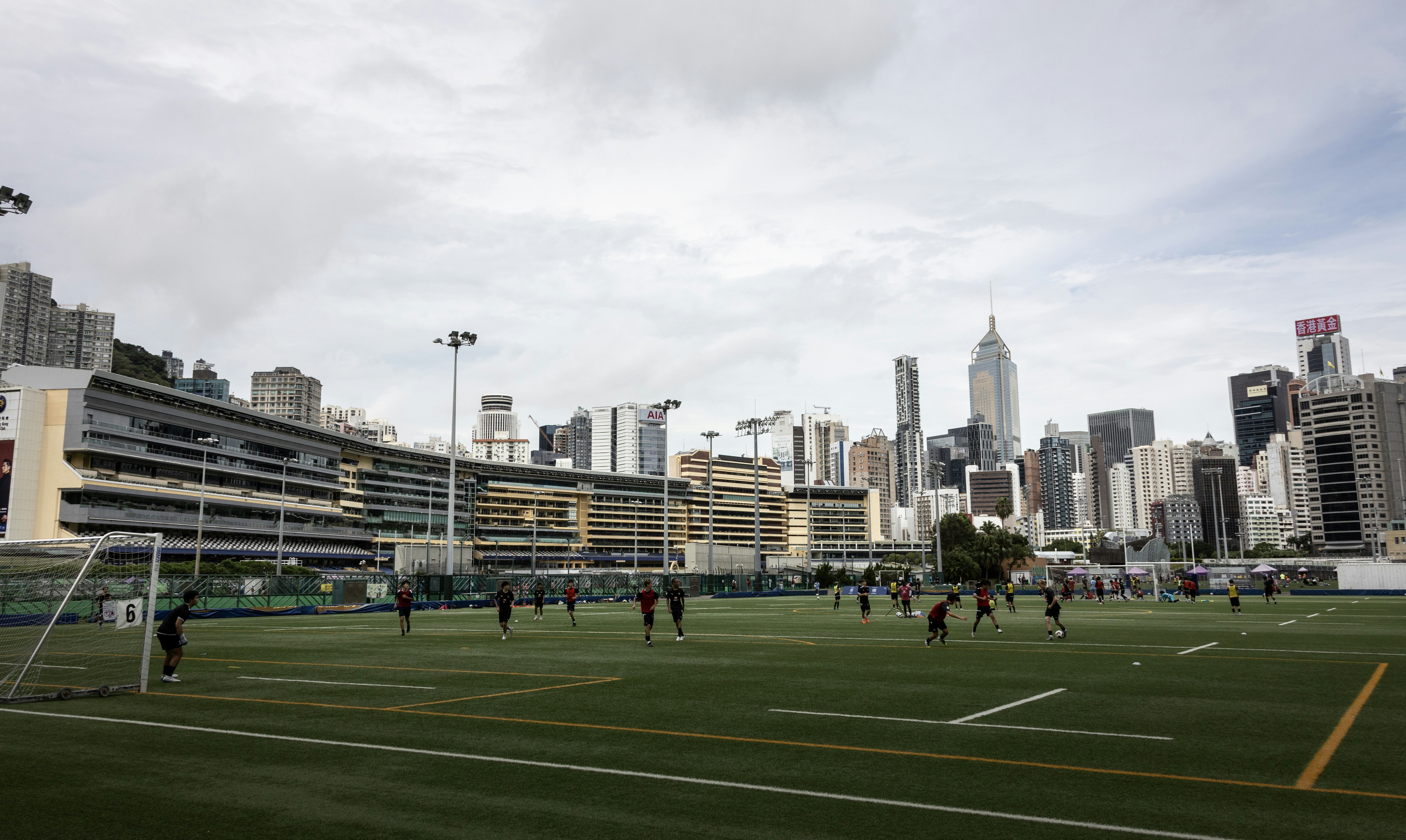 Pessoas jogando futebol em um campo verde em frente ao horizonte de Hong Kong