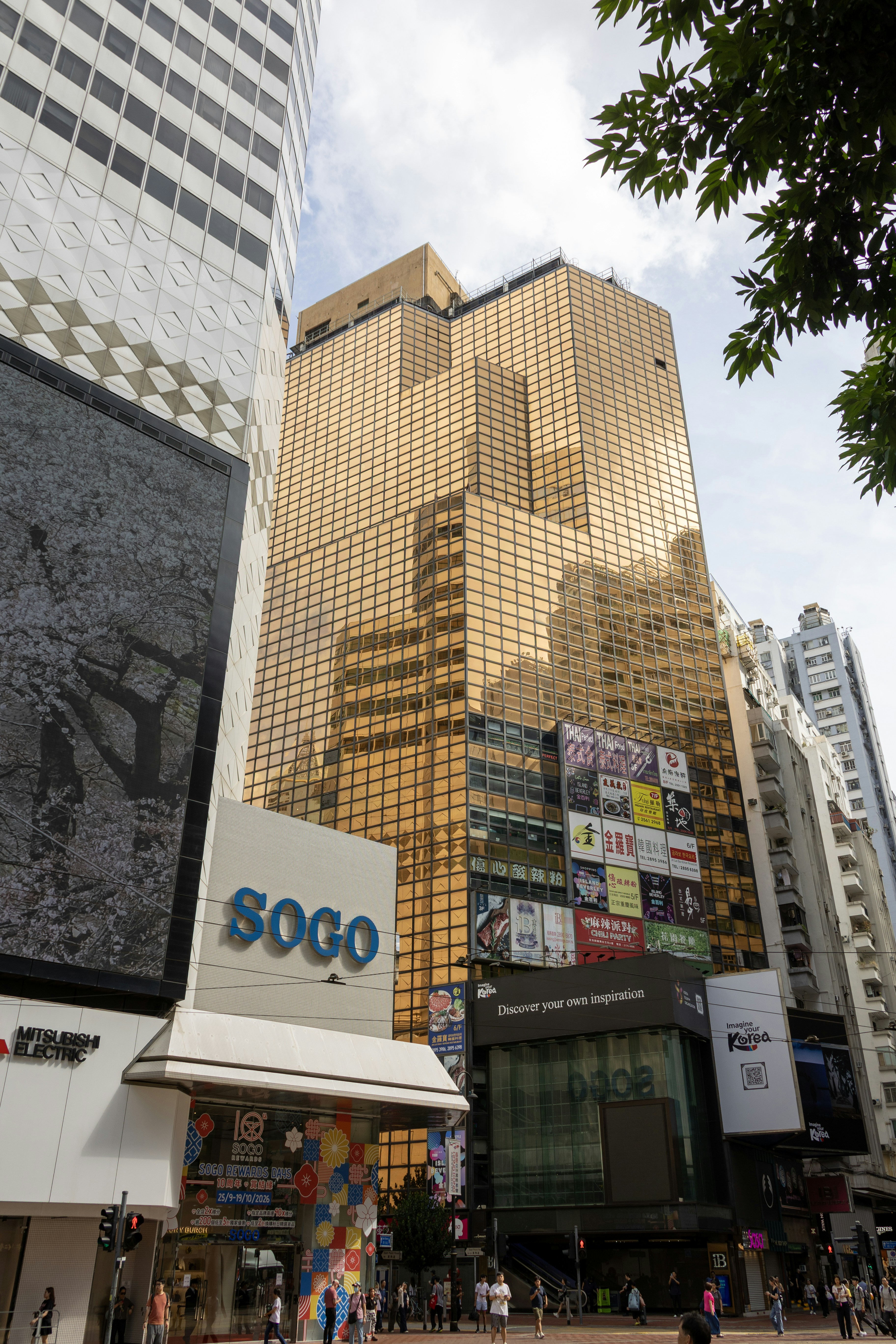 Um arranha-céu de vidro dourado se ergue acima da loja de departamentos Sogo, em Hong Kong