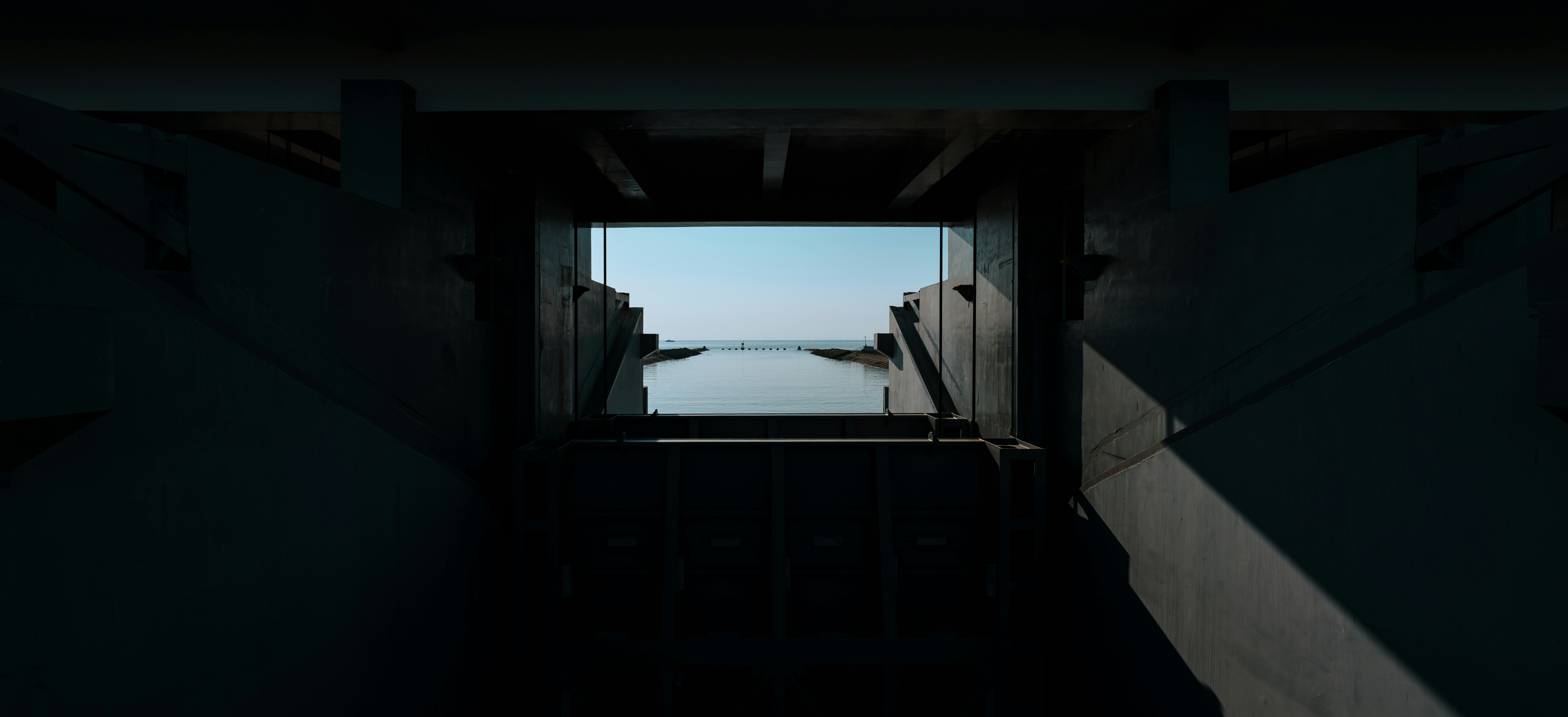 A view of the sea through a dark concrete floodgate structure