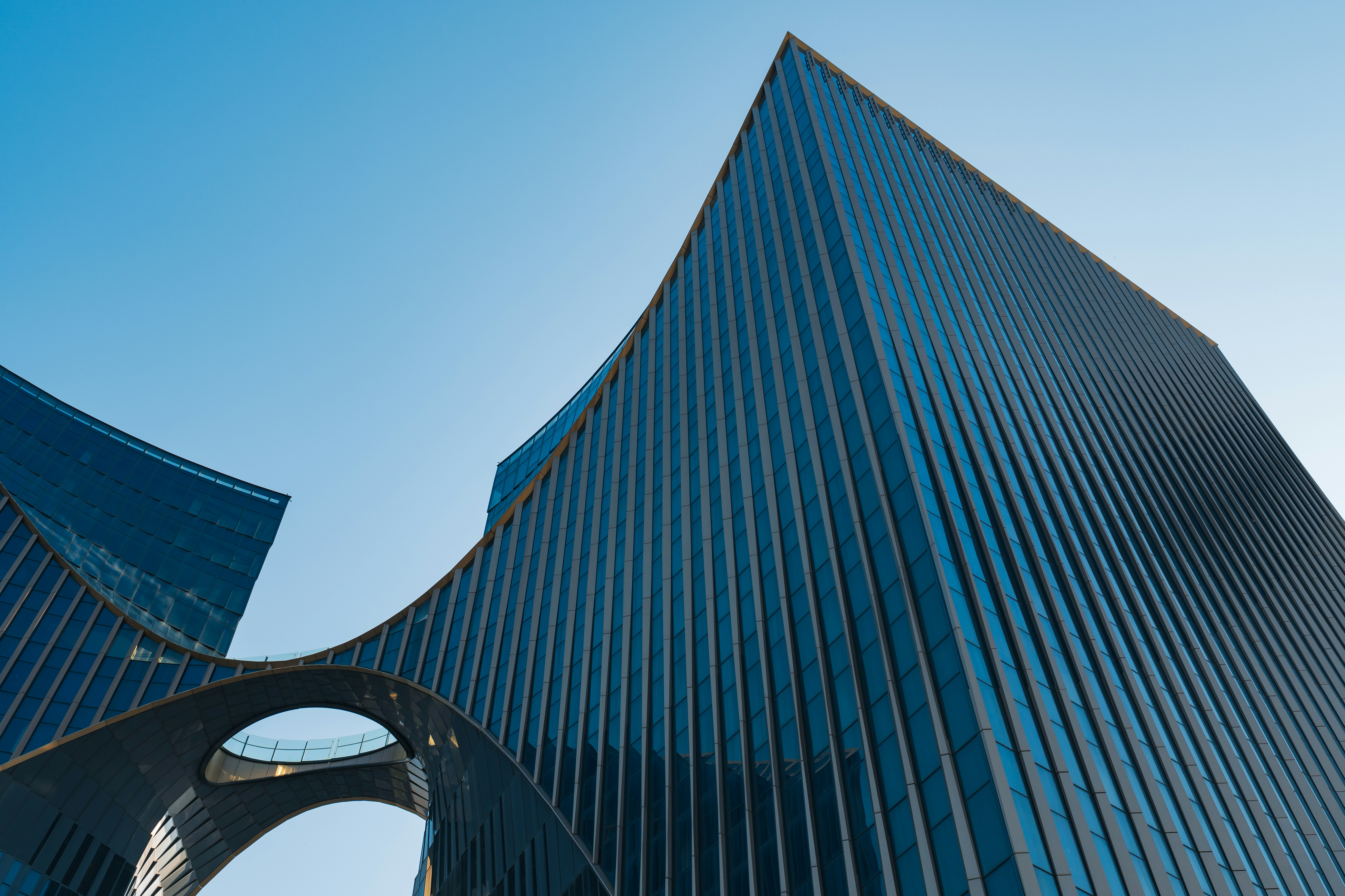 Modern glass skyscrapers with a curved bridge connecting the two towers against blue sky