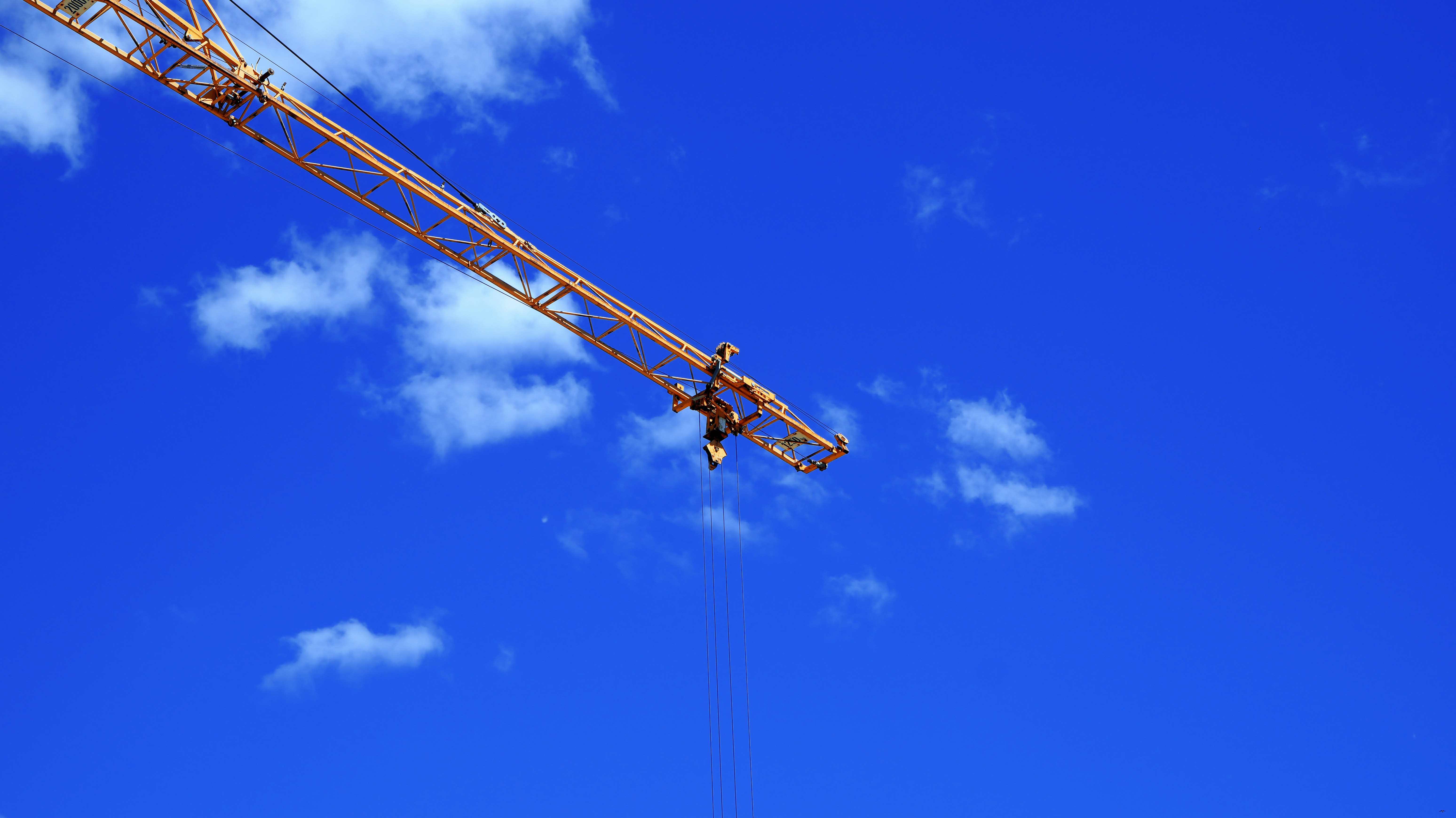 A yellow construction crane jib against a bright blue sky with white clouds