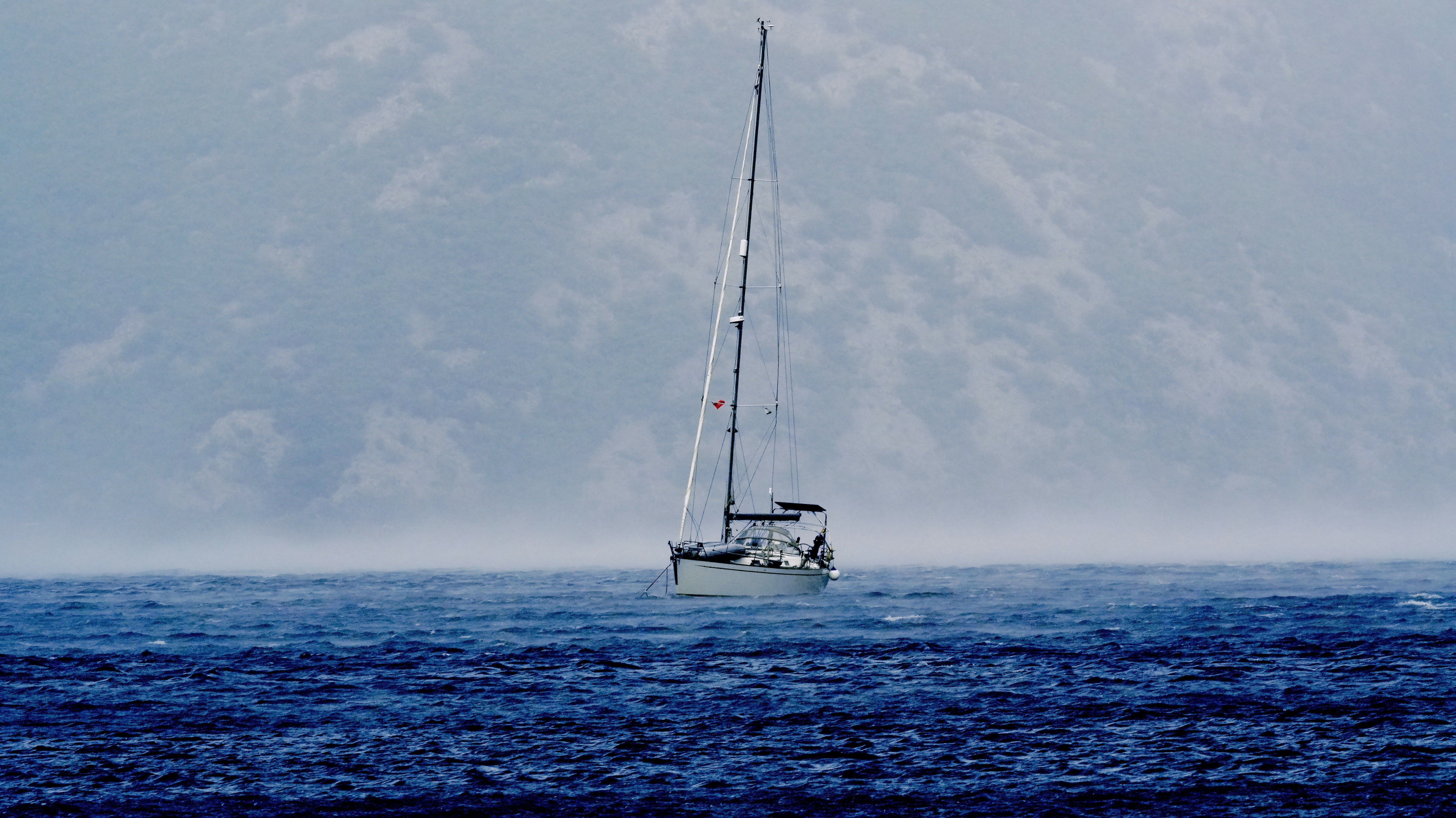 A sailboat on choppy dark blue water before a misty mountain backdrop