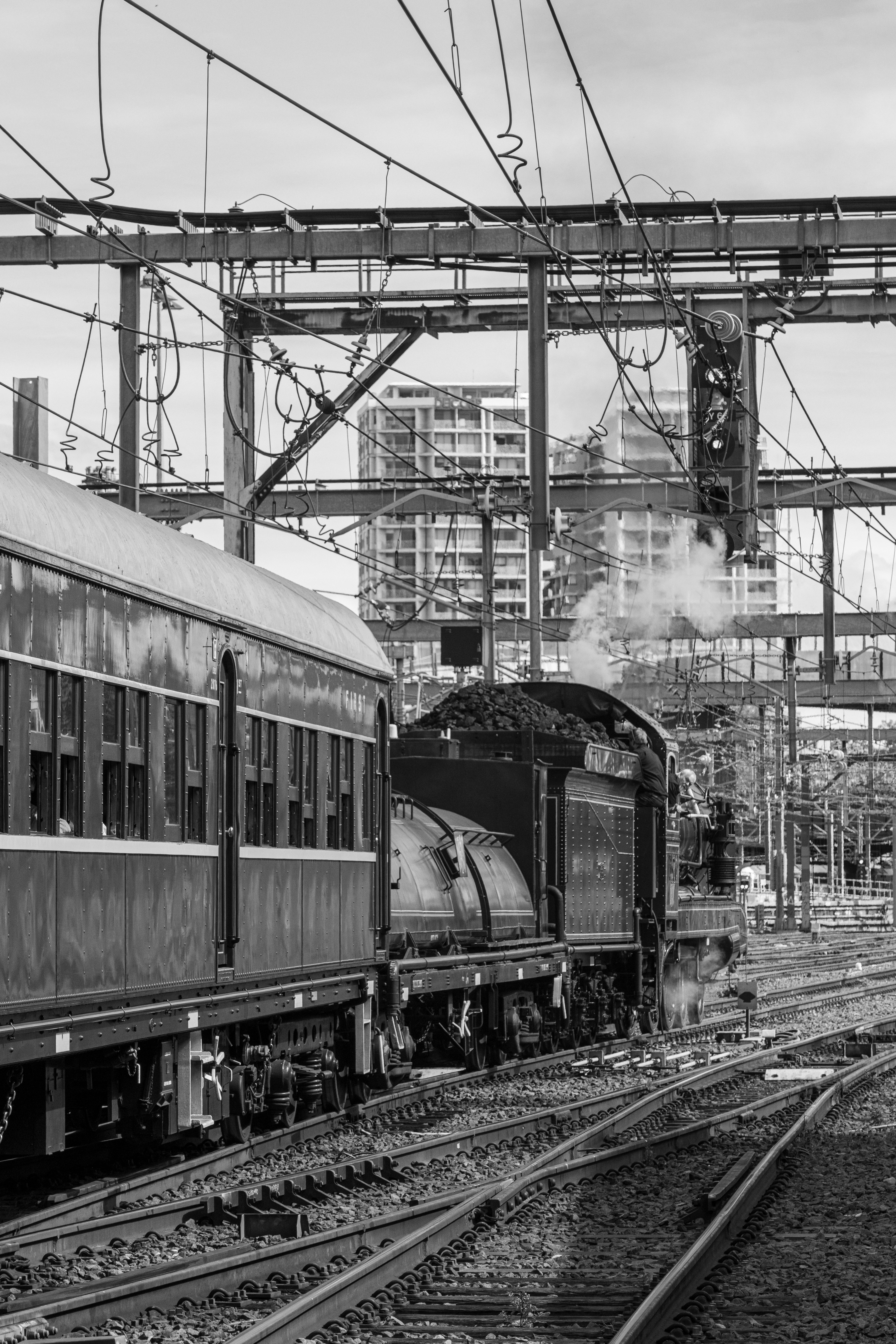 A steam locomotive pulling a passenger carriage on tracks beneath overhead electrical wires