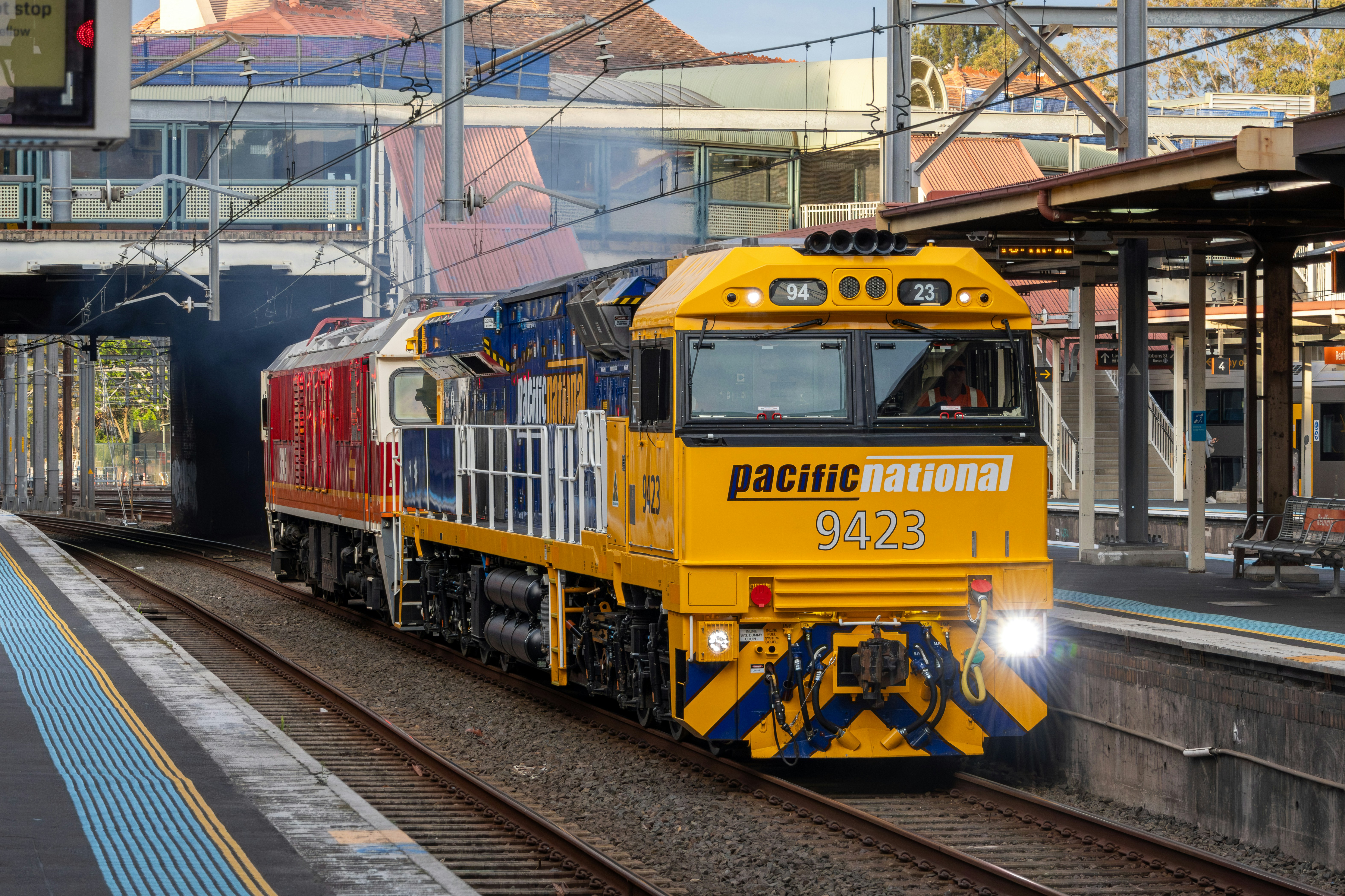 A yellow and blue diesel locomotive pulling a red train through a station