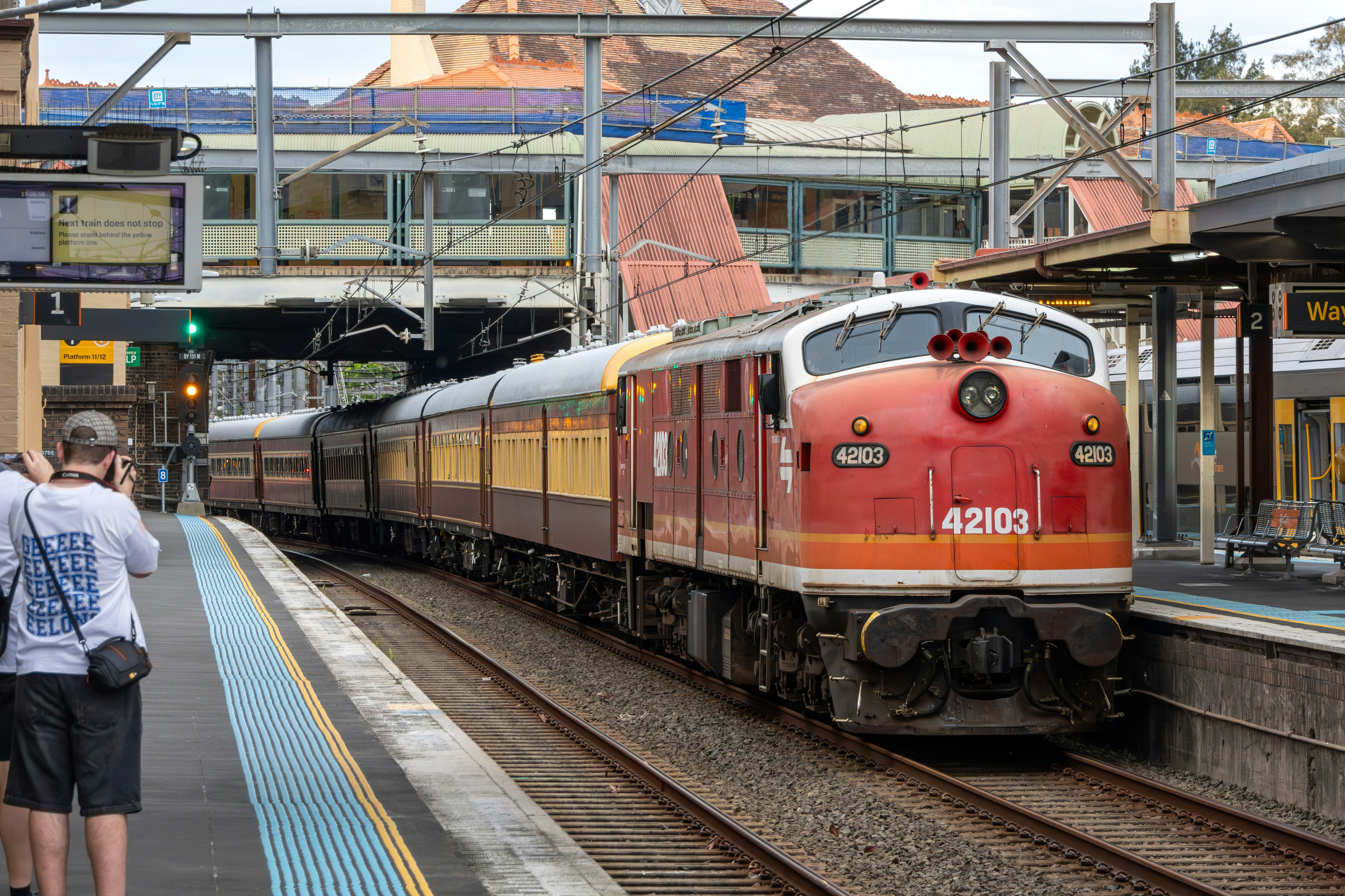 A person photographing a red and yellow vintage train at a railway station