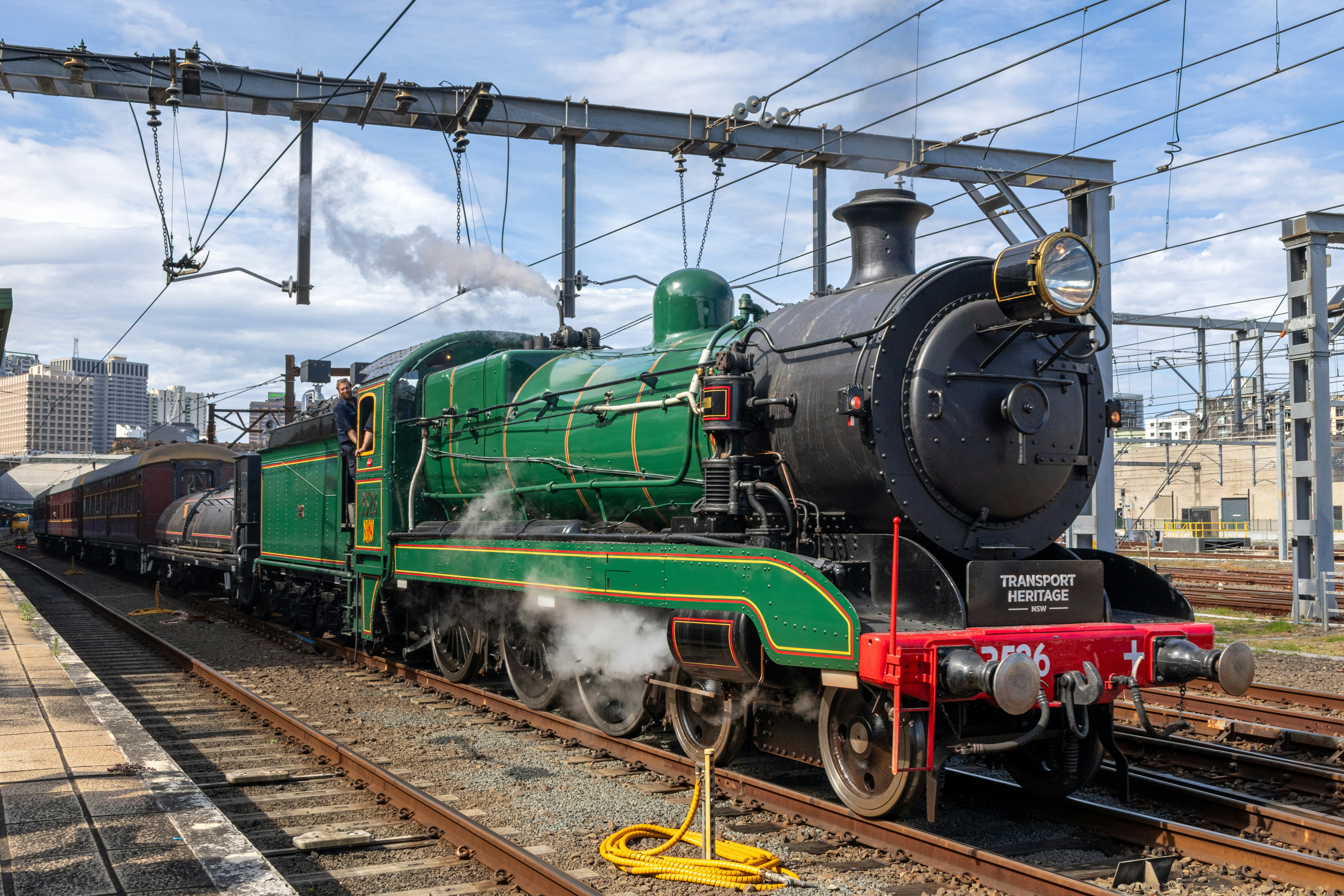 A green steam locomotive pulling passenger carriages at a railway station
