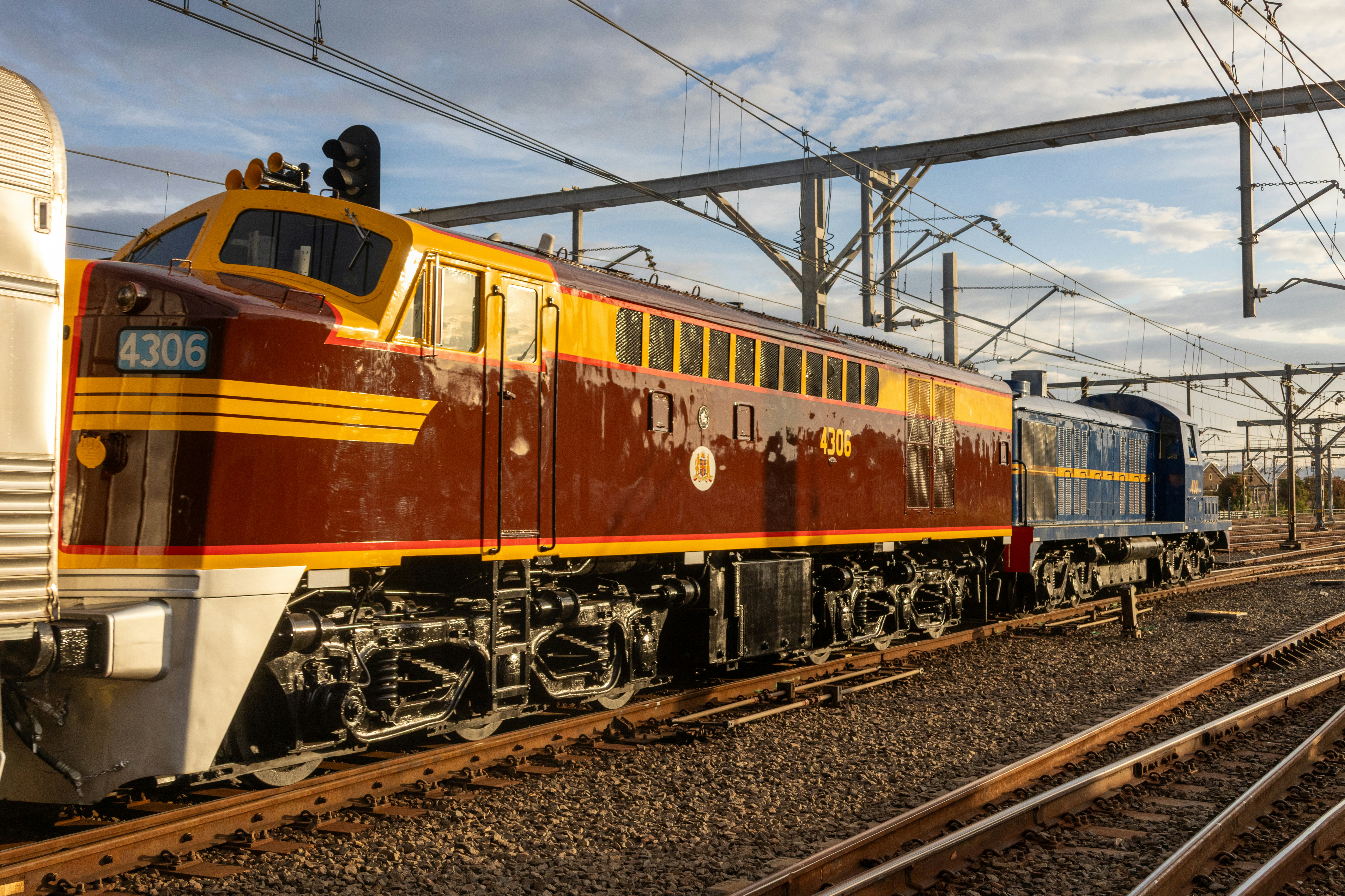 A brown and yellow diesel locomotive on railway tracks under overhead power lines