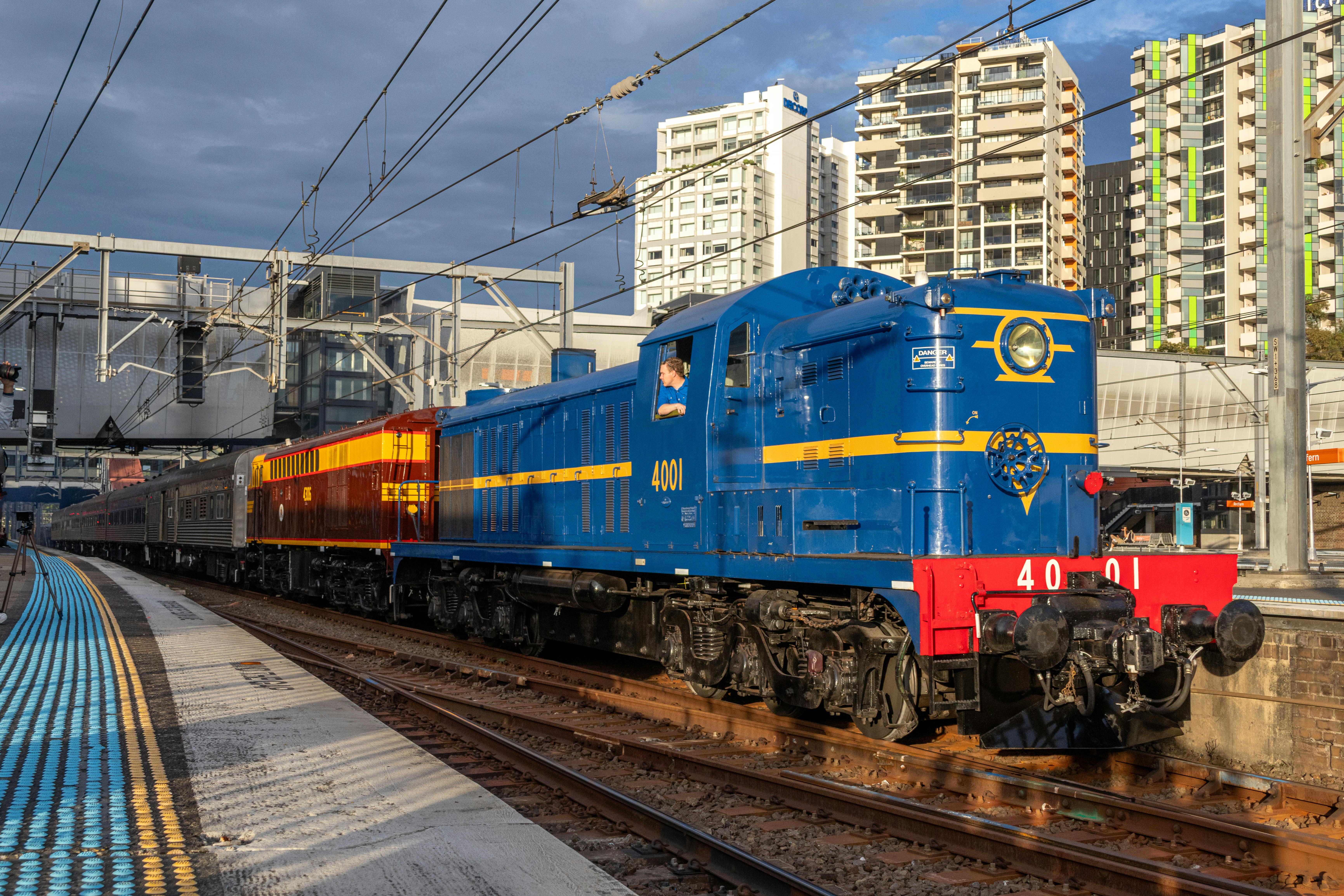 A blue diesel locomotive pulling passenger carriages through a city train station