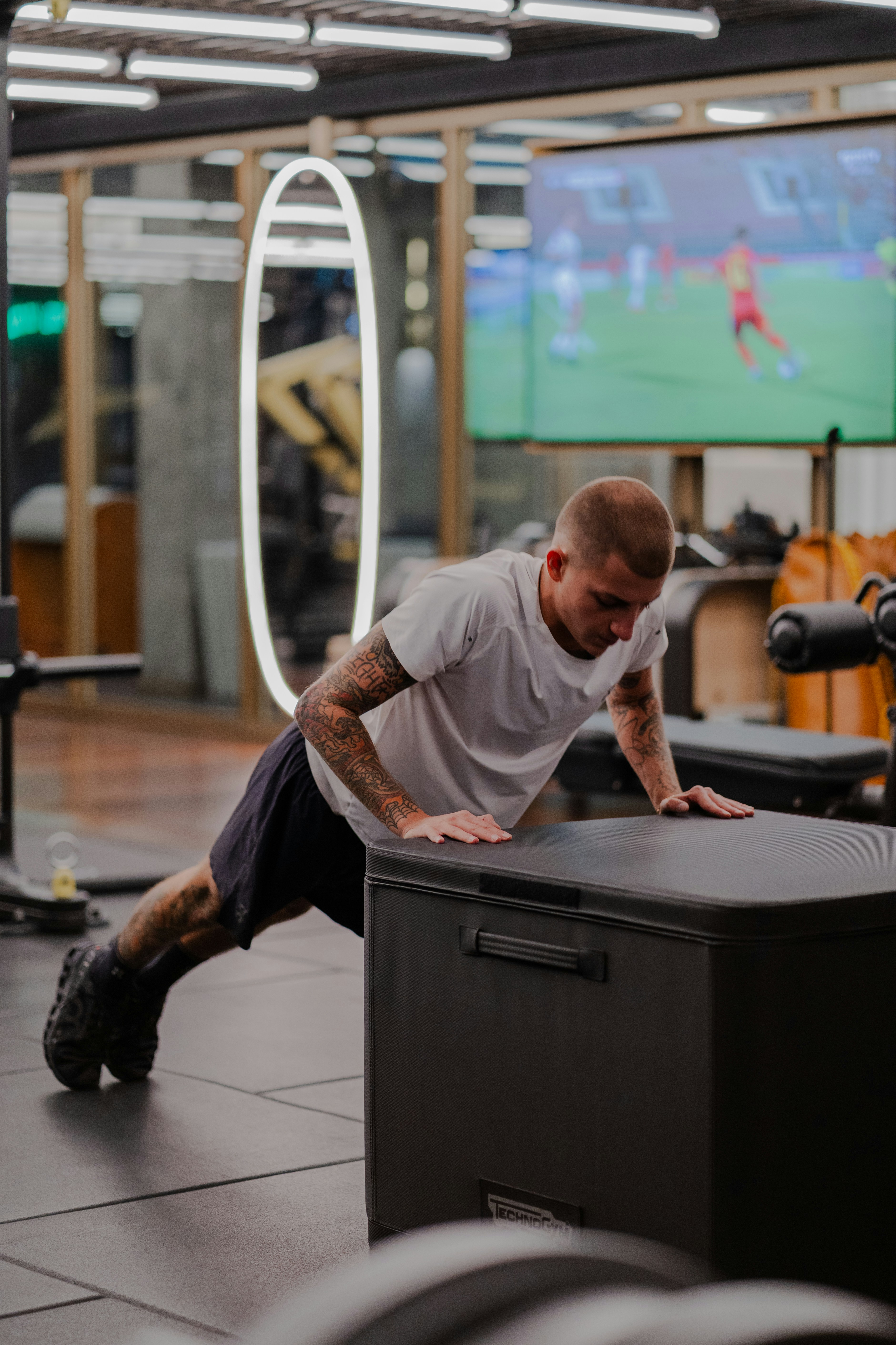 A tattooed man in a white t-shirt doing push-ups on a black box