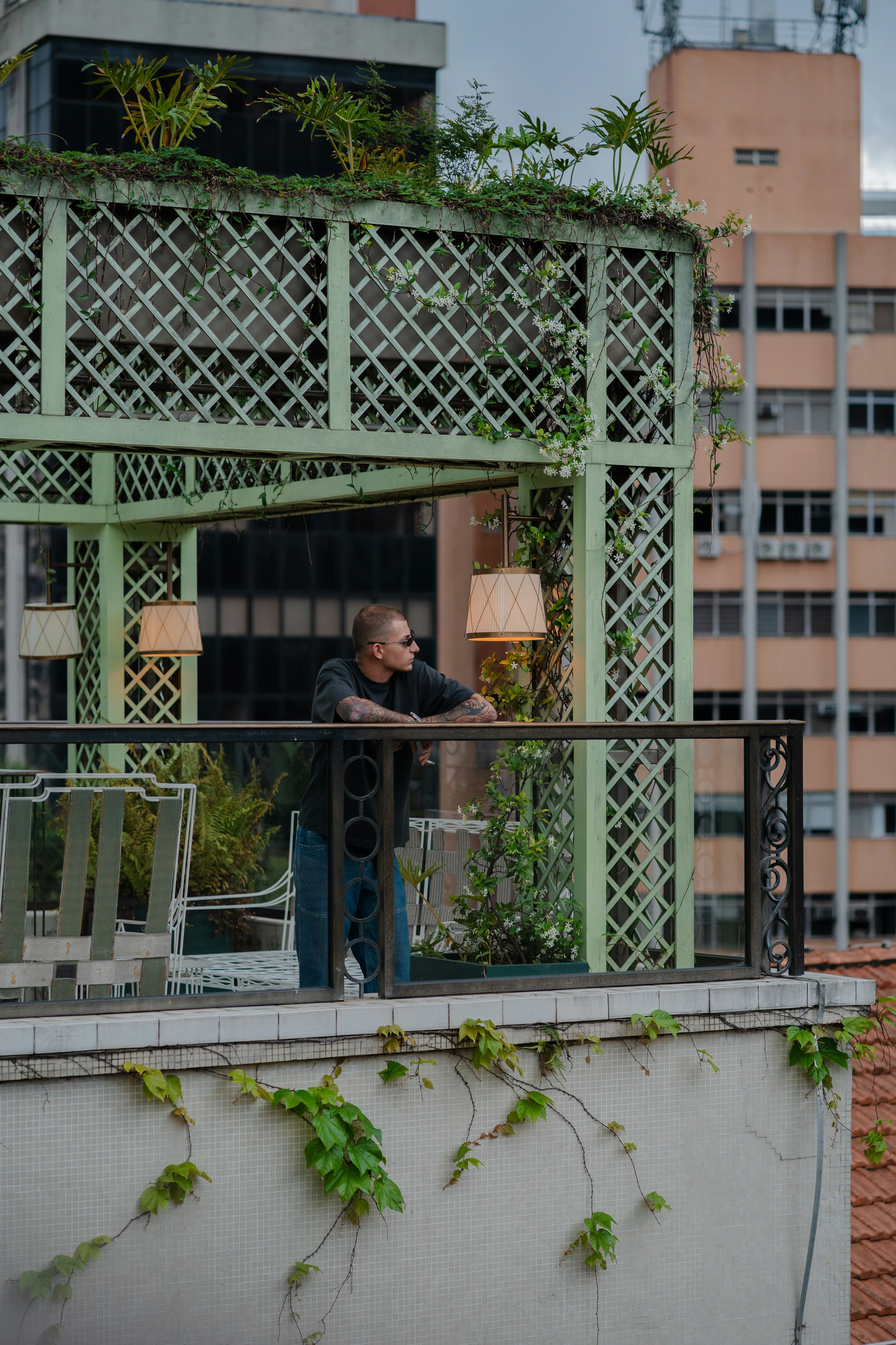 A person with tattoos leaning on a railing in a green rooftop gazebo