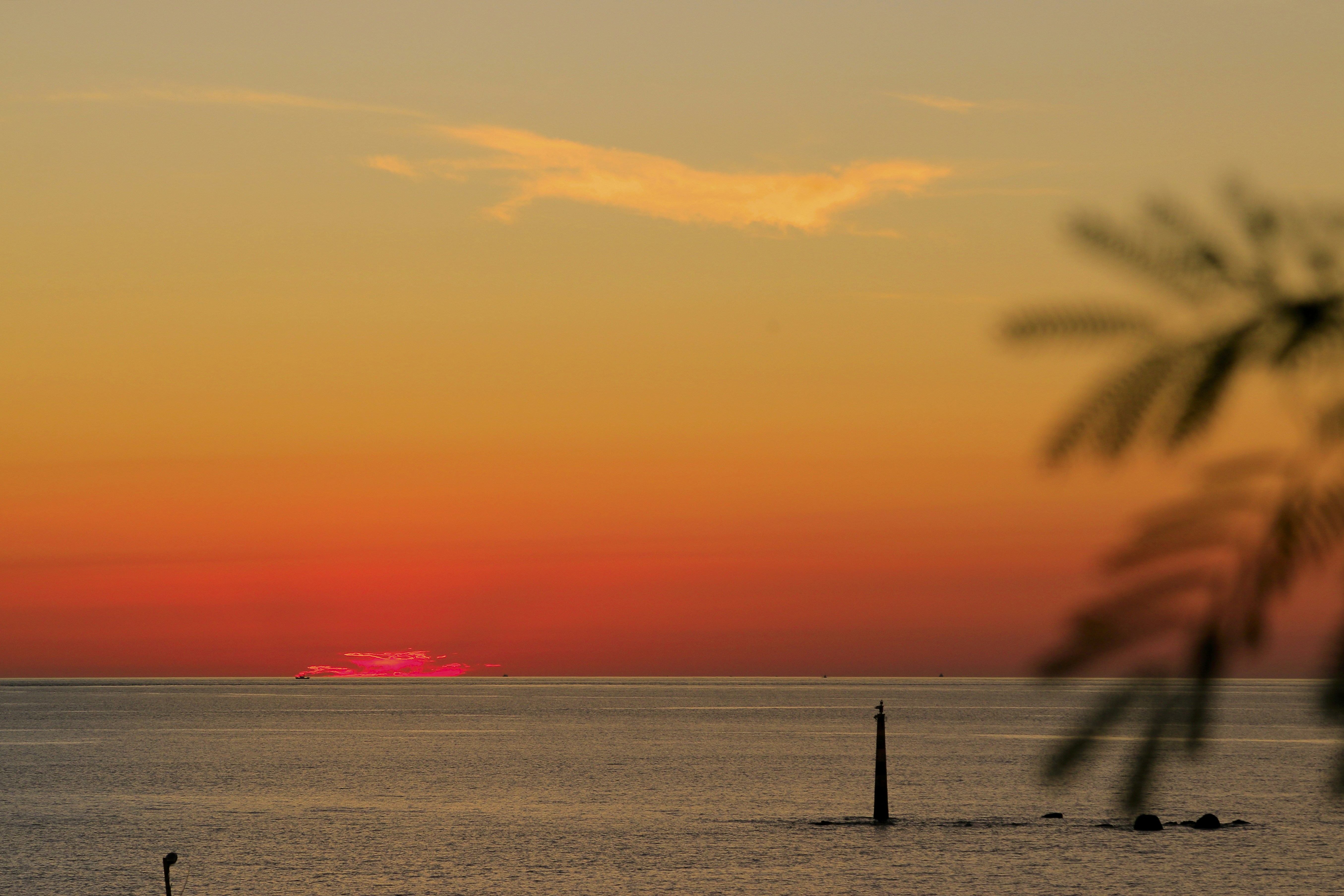 A lone beacon in the calm sea under a vibrant orange sky