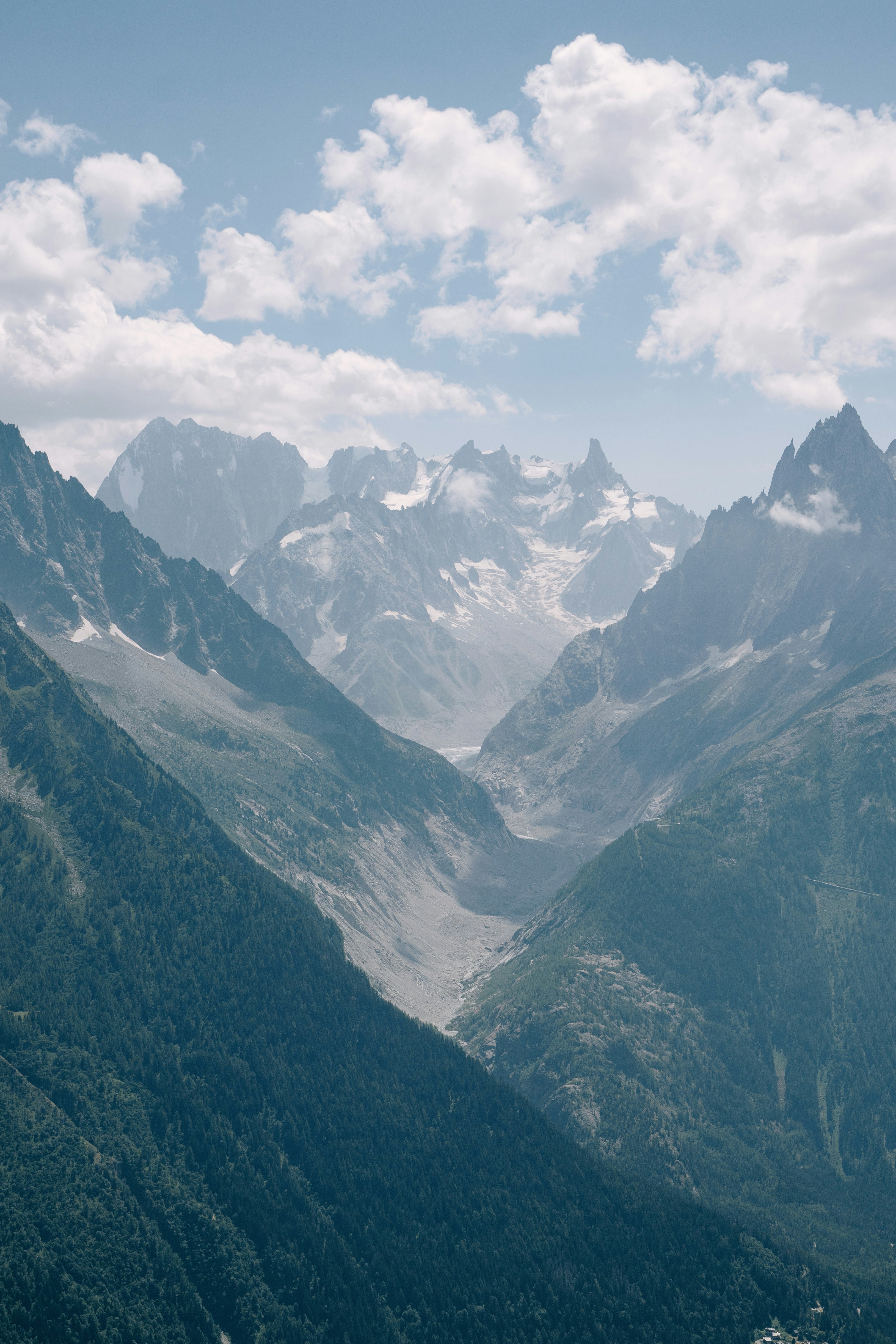 A deep valley between steep forested mountains leading to snow-capped peaks under clouds