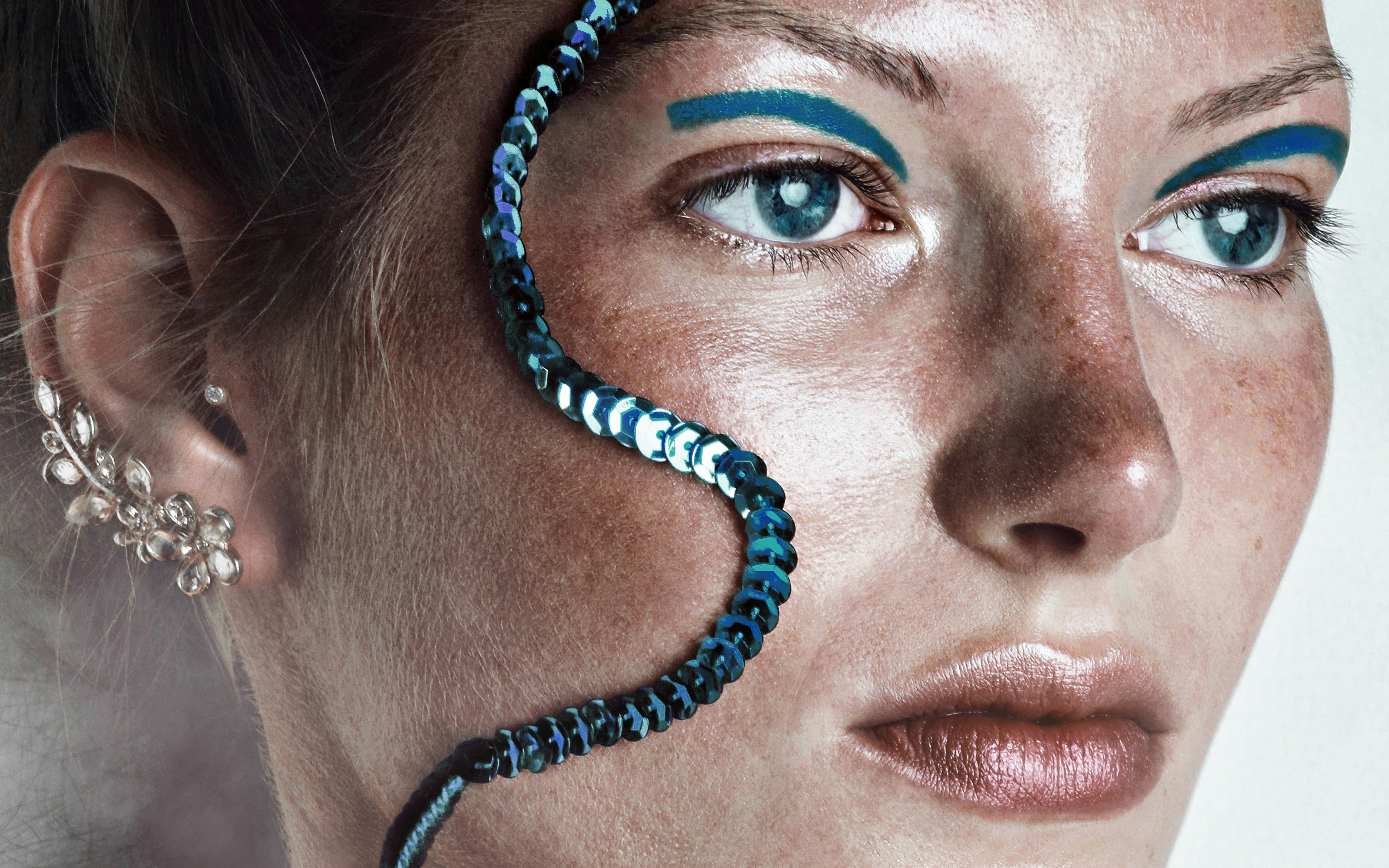 A woman with blue eyeshadow and a sequin strand across her face
