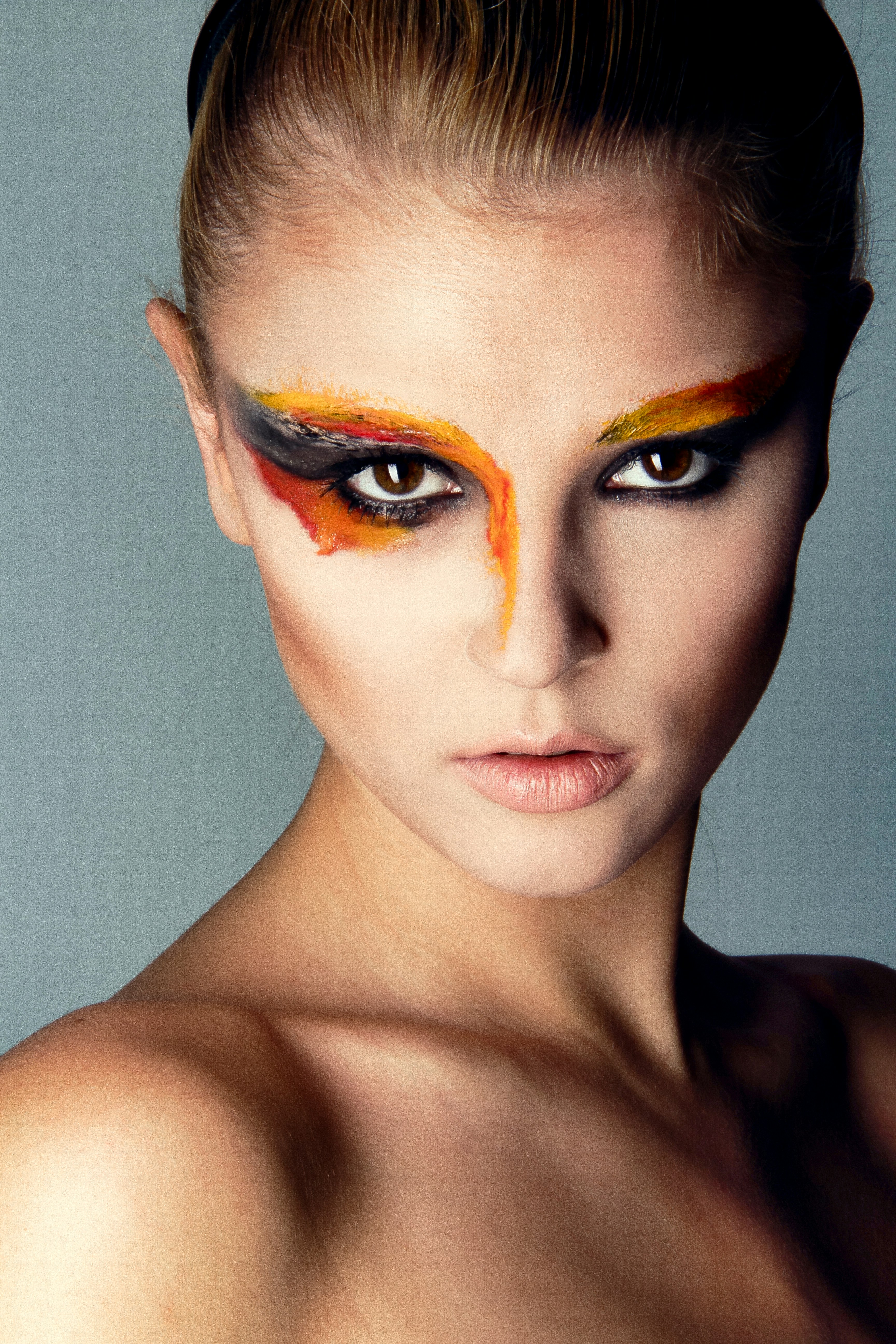 A woman with bold orange and black artistic eye makeup against a grey background