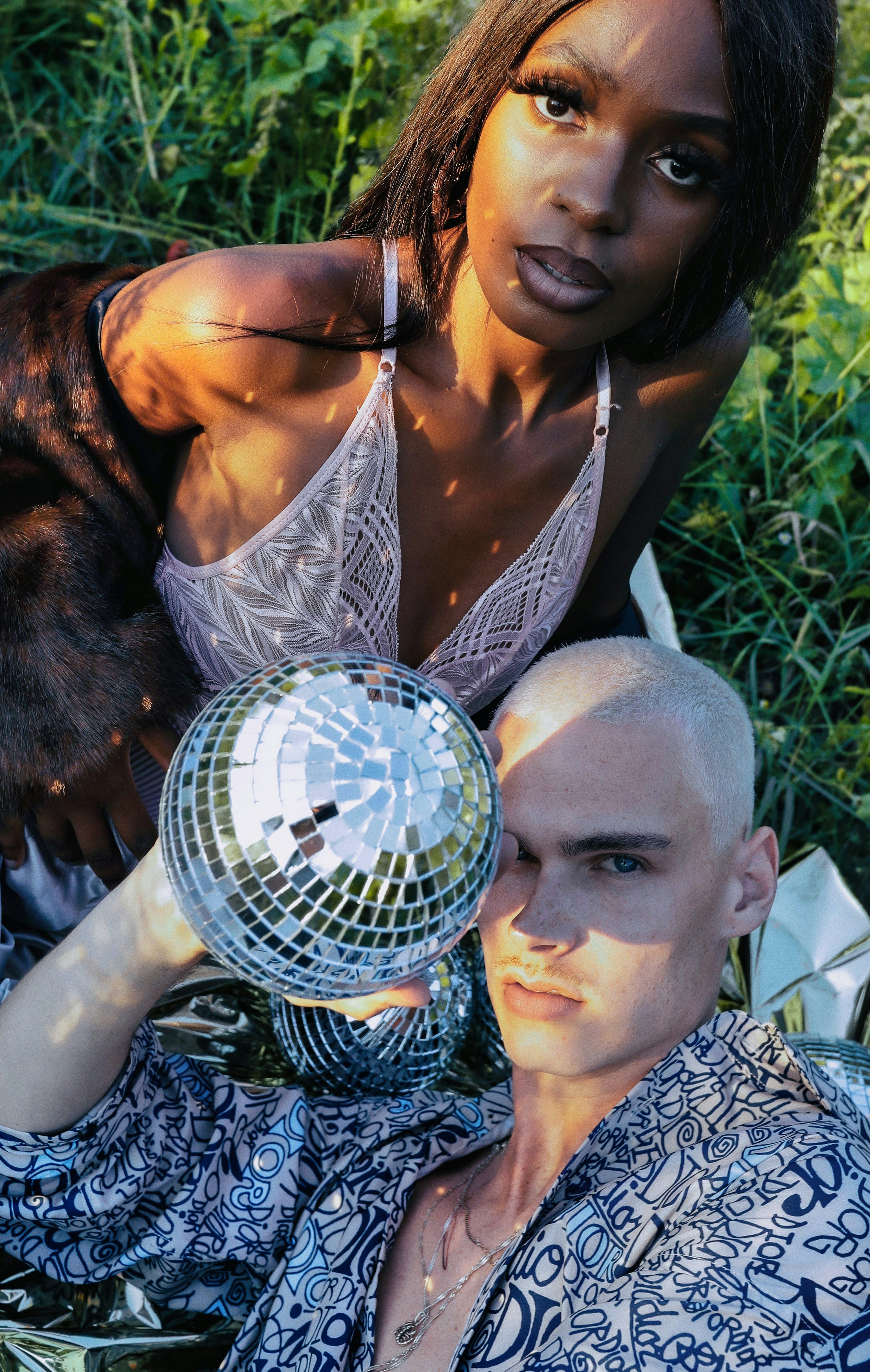 A woman and a man with a disco ball in a grassy field