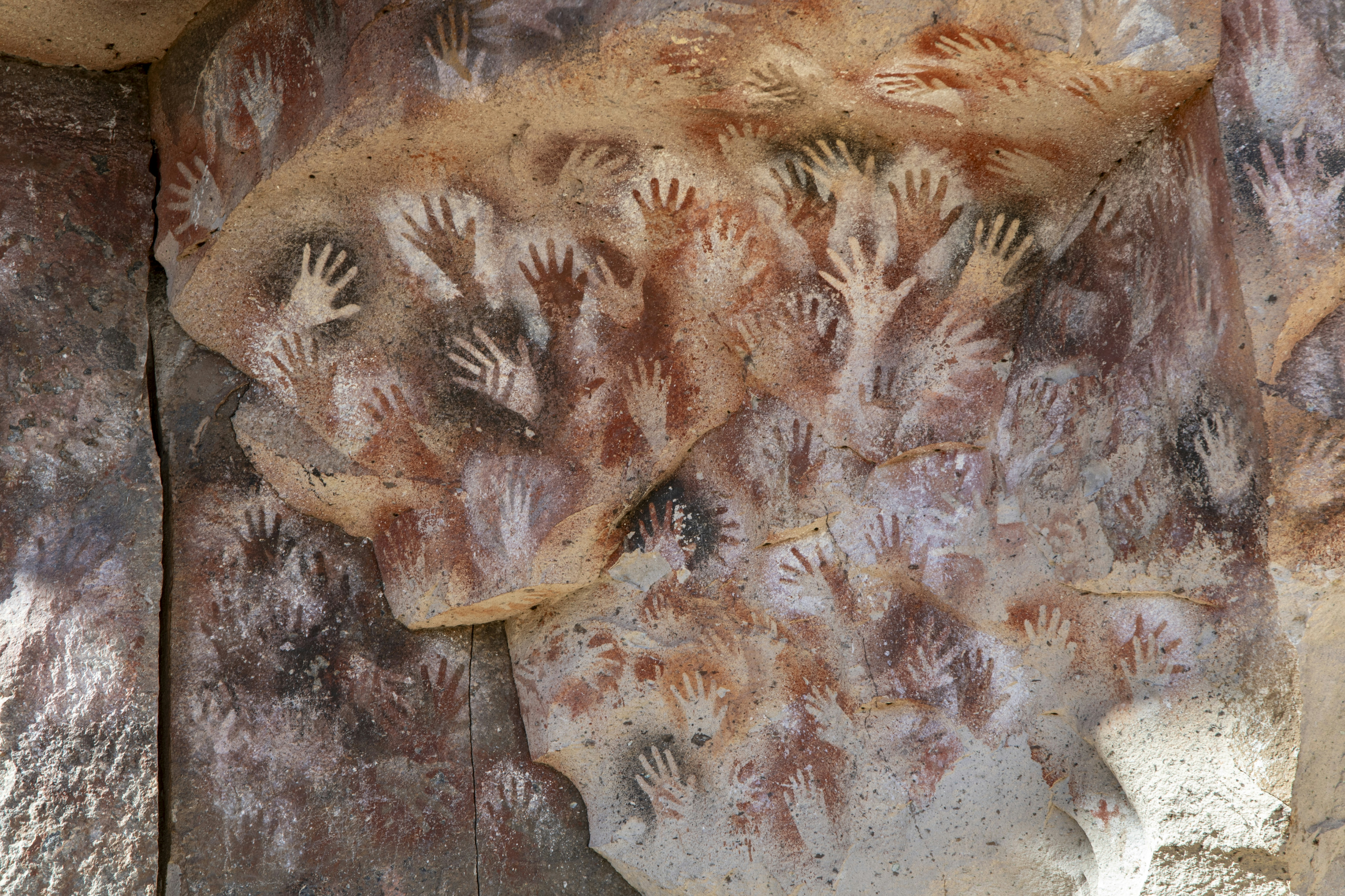 Red and white hand stencils painted on a textured rock wall