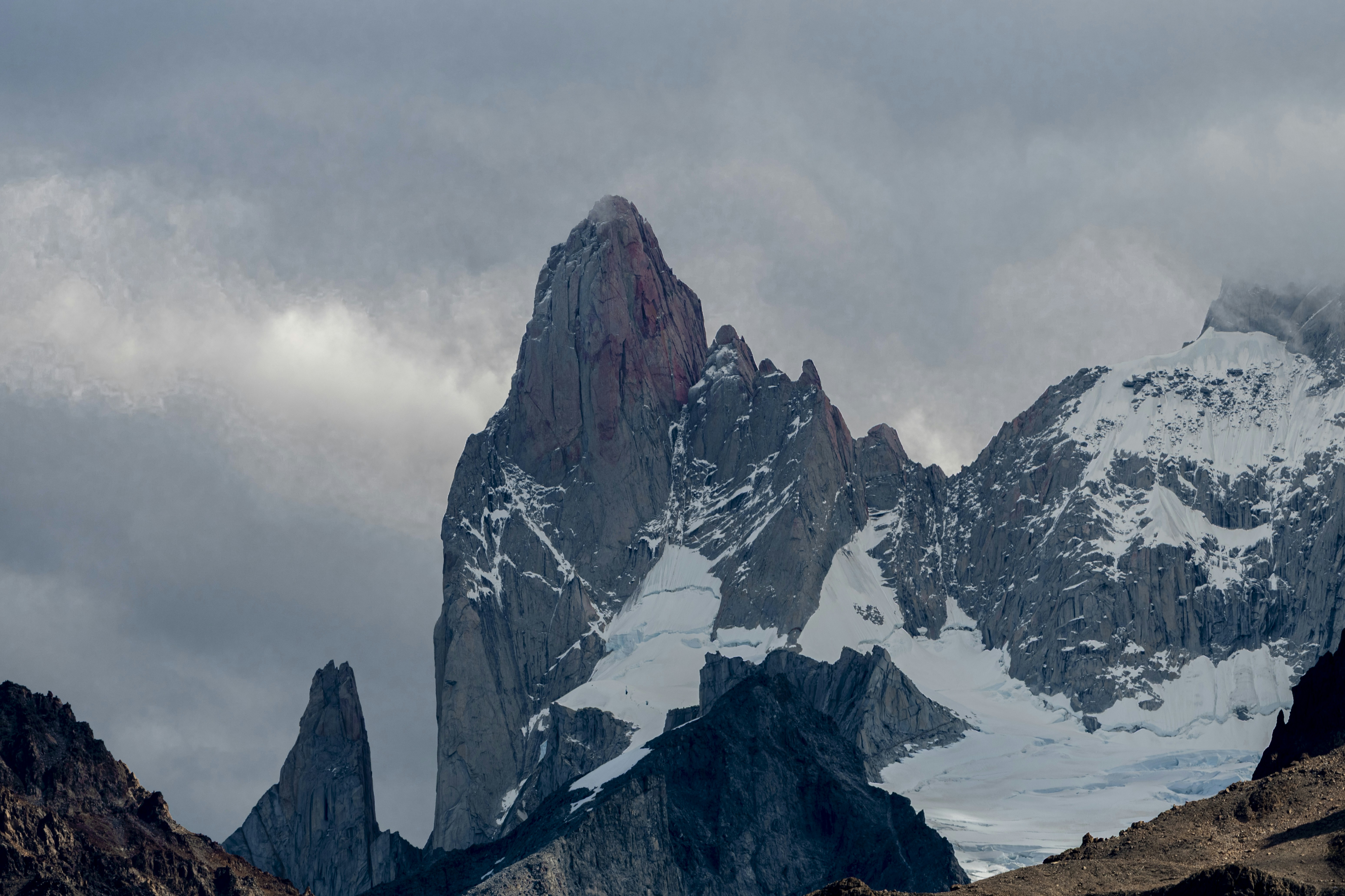 A jagged snow-capped mountain peak rising through heavy grey clouds