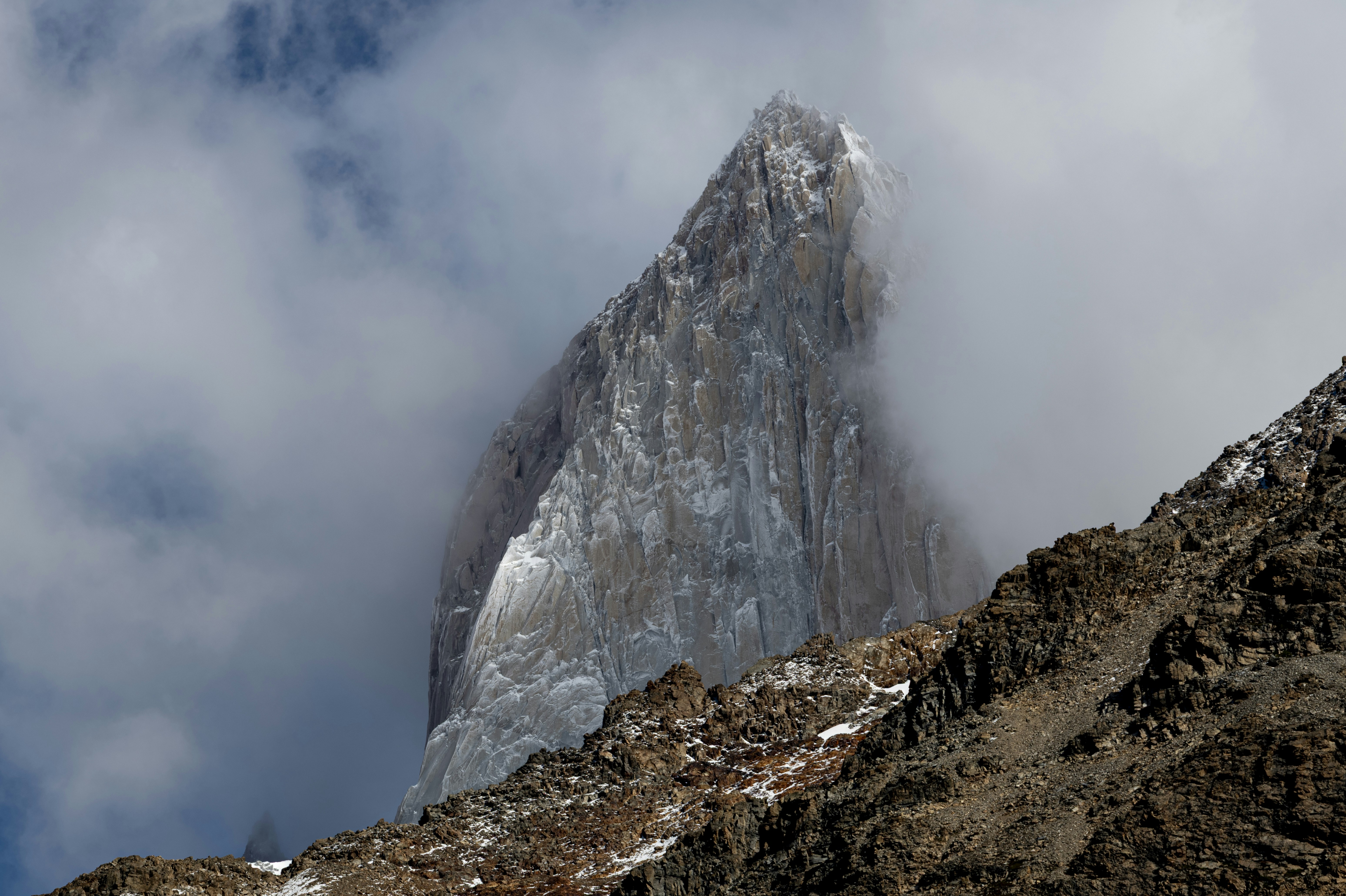 A jagged snow-covered mountain peak partially obscured by thick white clouds