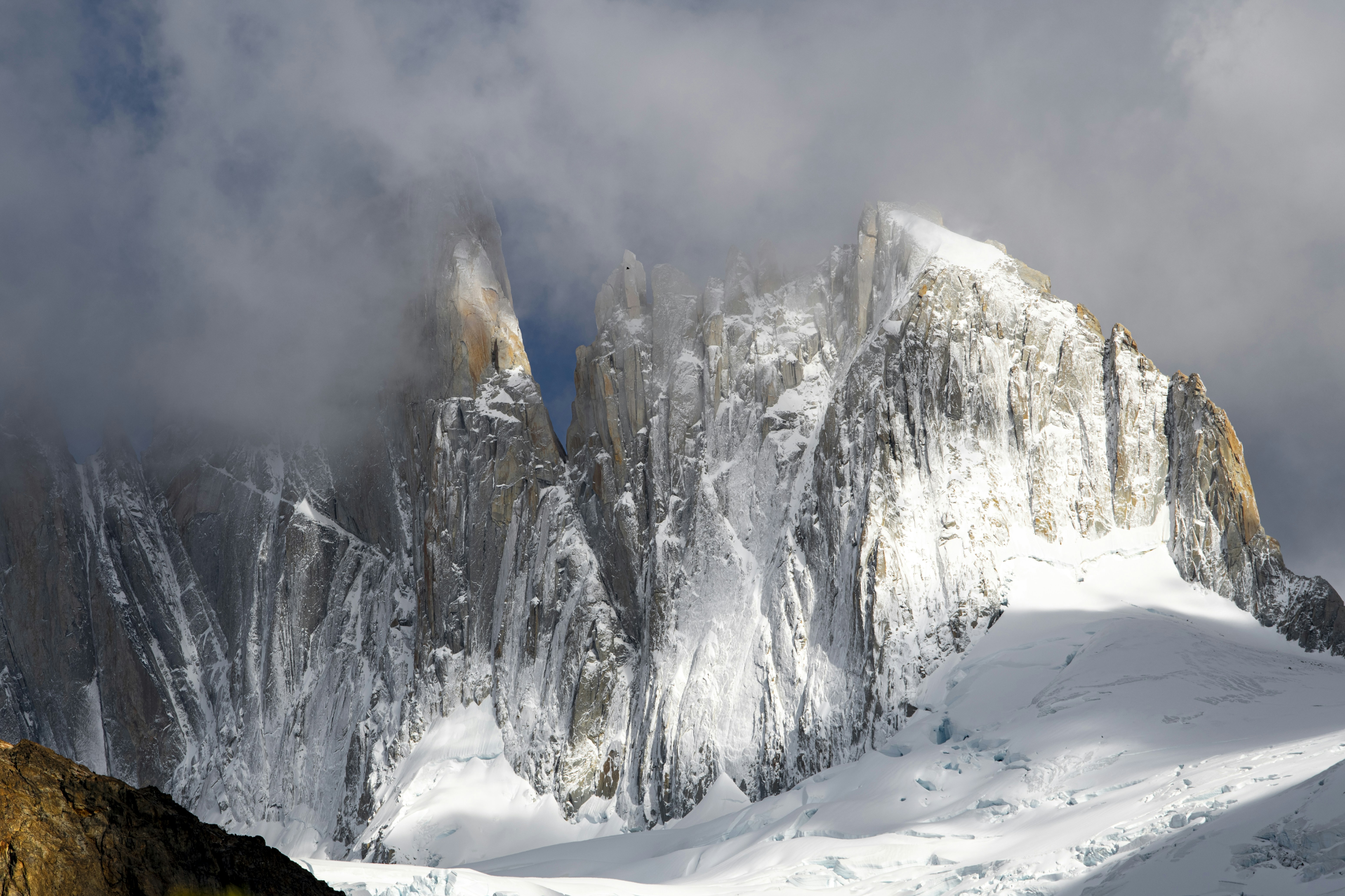 Snow-covered granite peaks rising through thick clouds under a bright sky