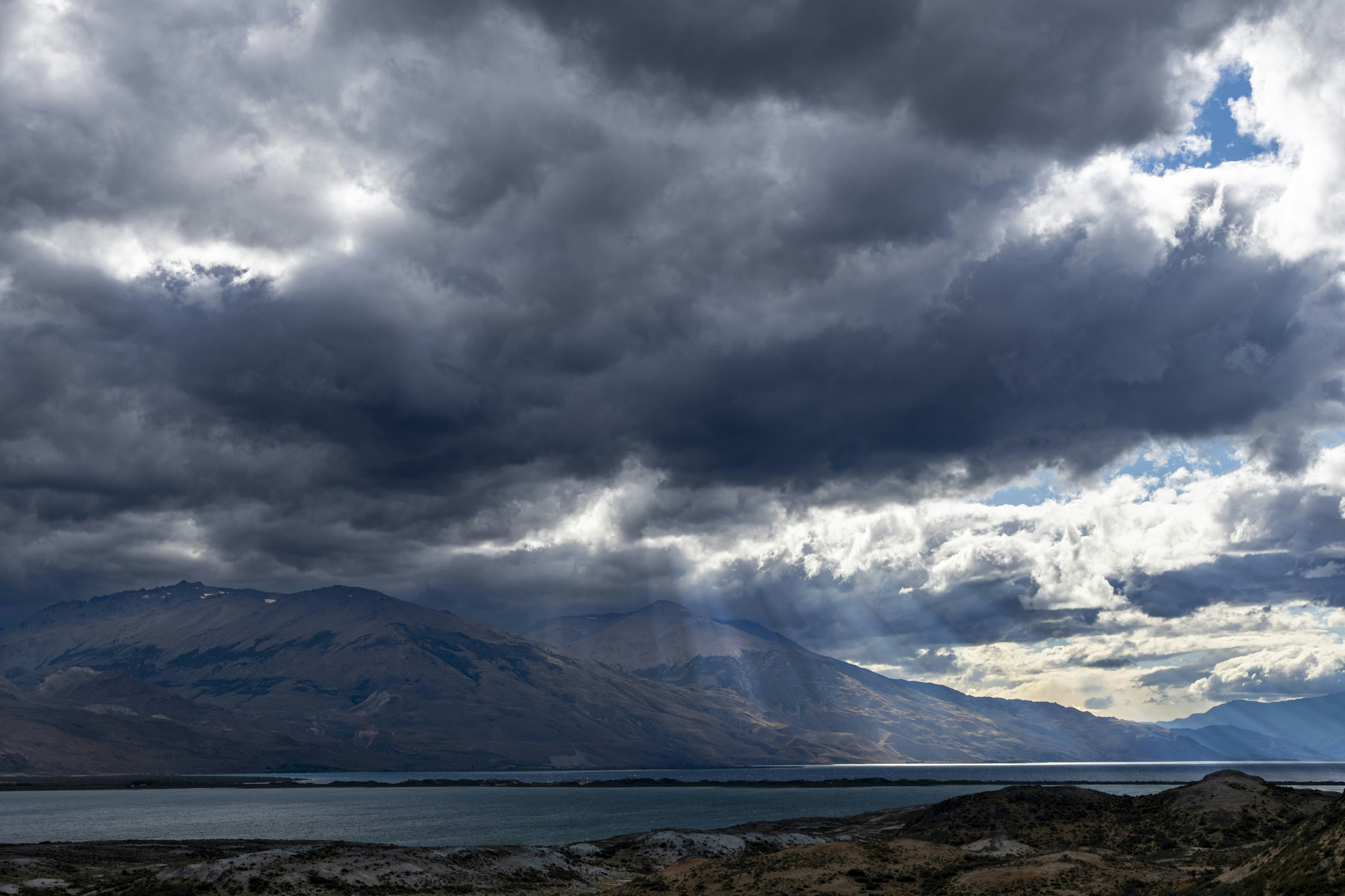 Sunlight breaking through dark storm clouds over a lake and distant mountains