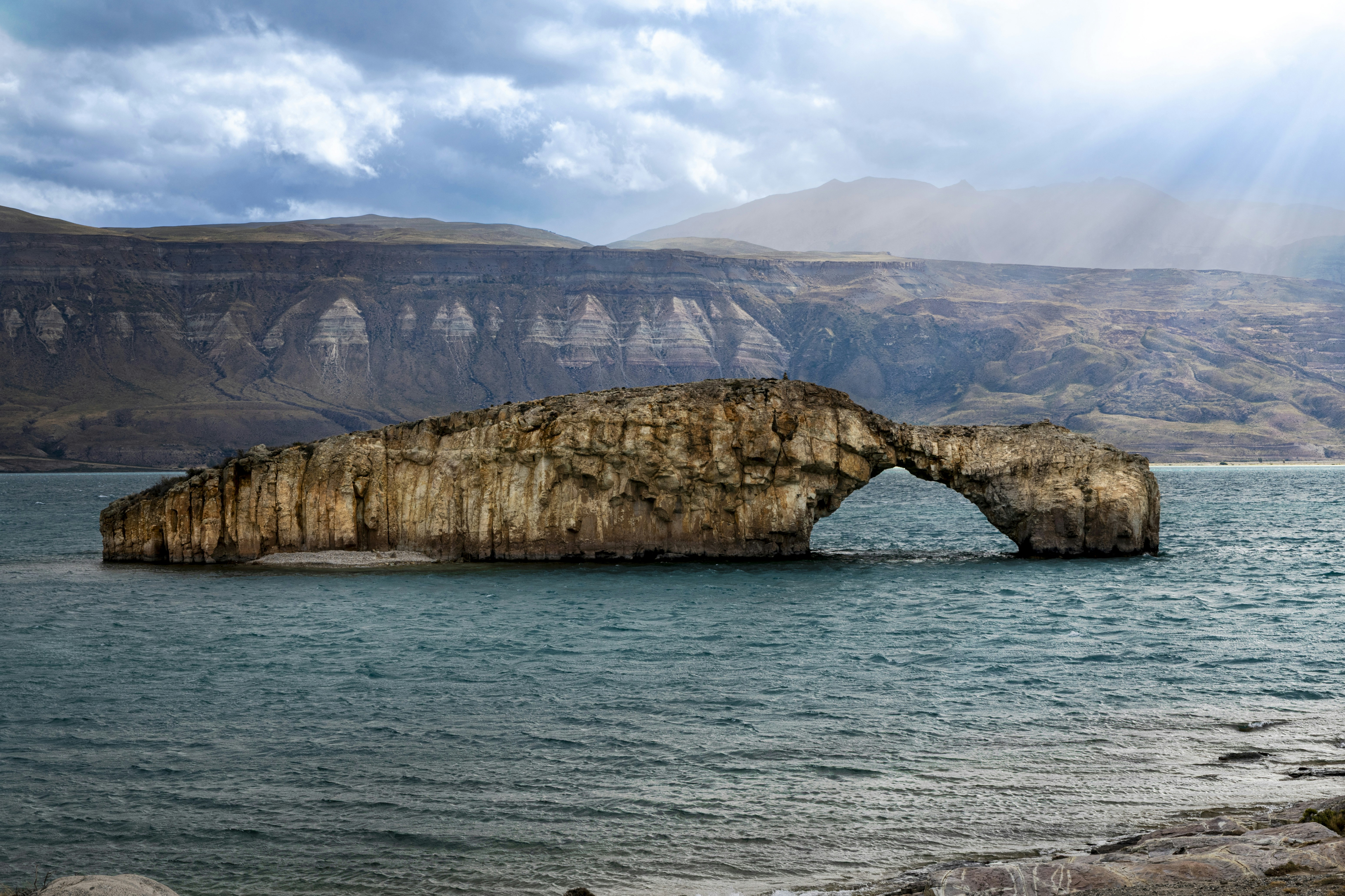 A natural stone arch on a rocky island in a blue lake
