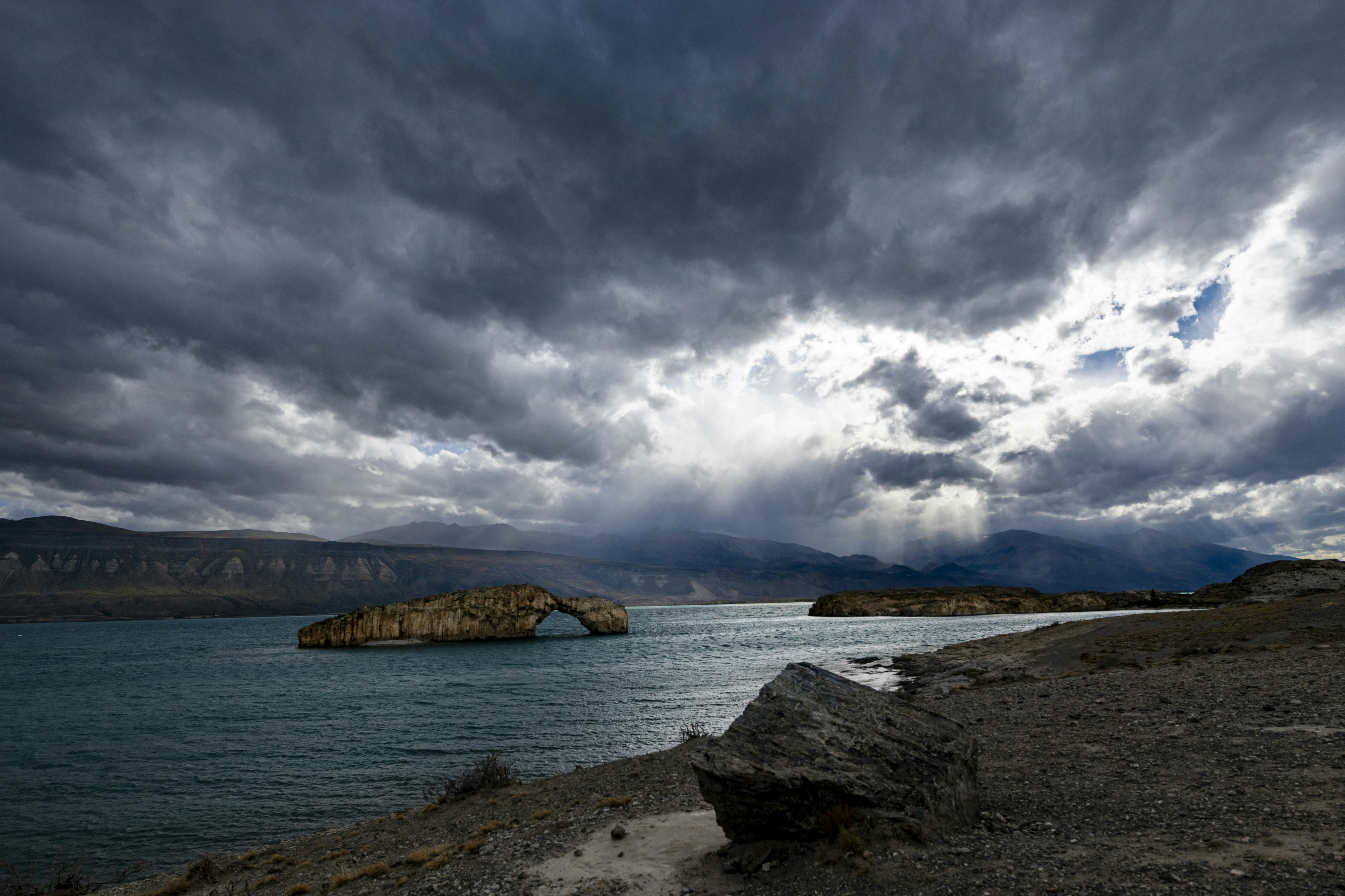 A natural stone arch in a lake under a dramatic cloudy sky