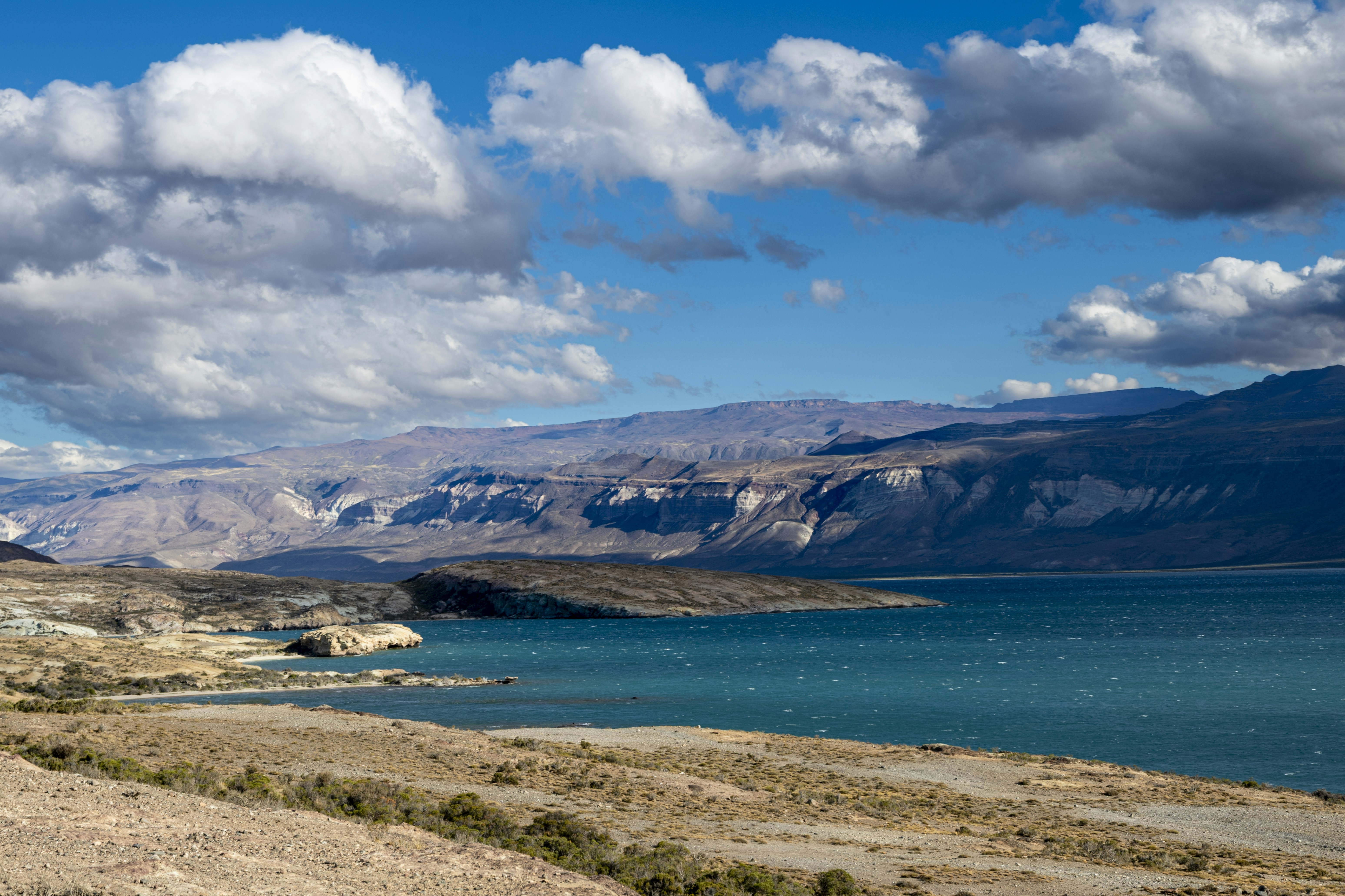 A turquoise lake surrounded by arid hills under a bright blue sky