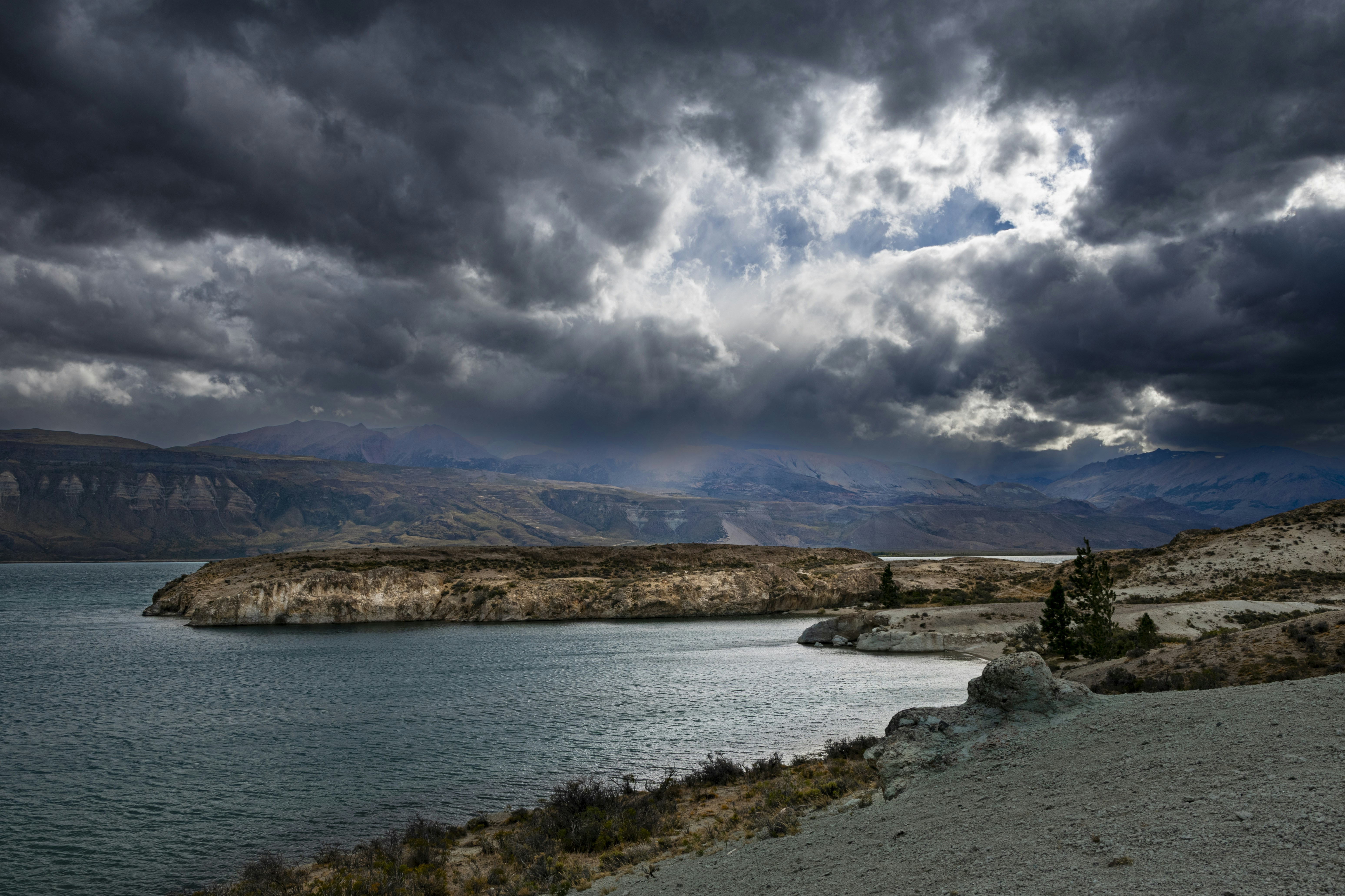 A turquoise lake under a dark stormy sky with mountains in the distance