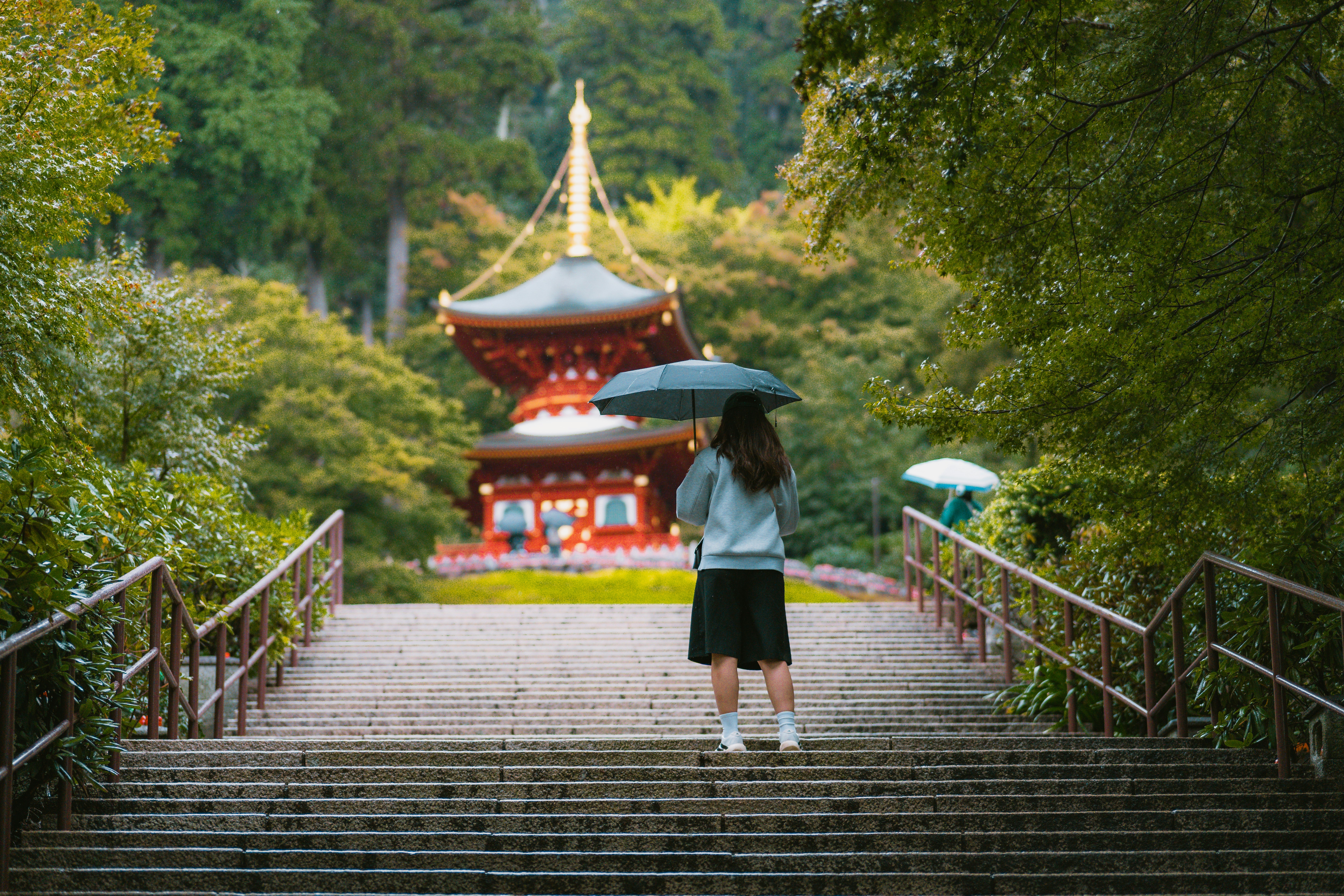A person with an umbrella on stone steps leading to a red pagoda