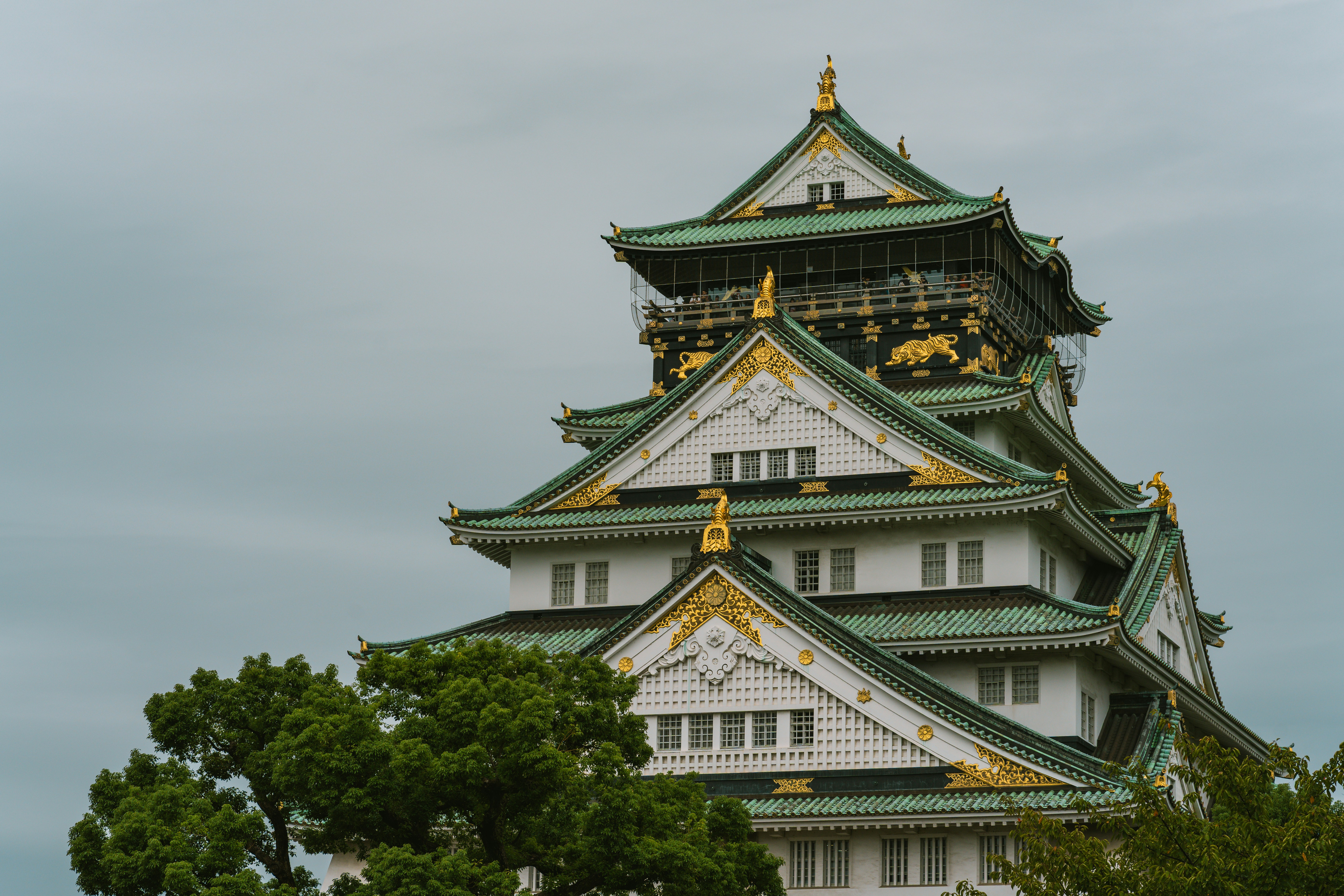 Osaka Castle with green tiled roofs and gold accents against a grey sky