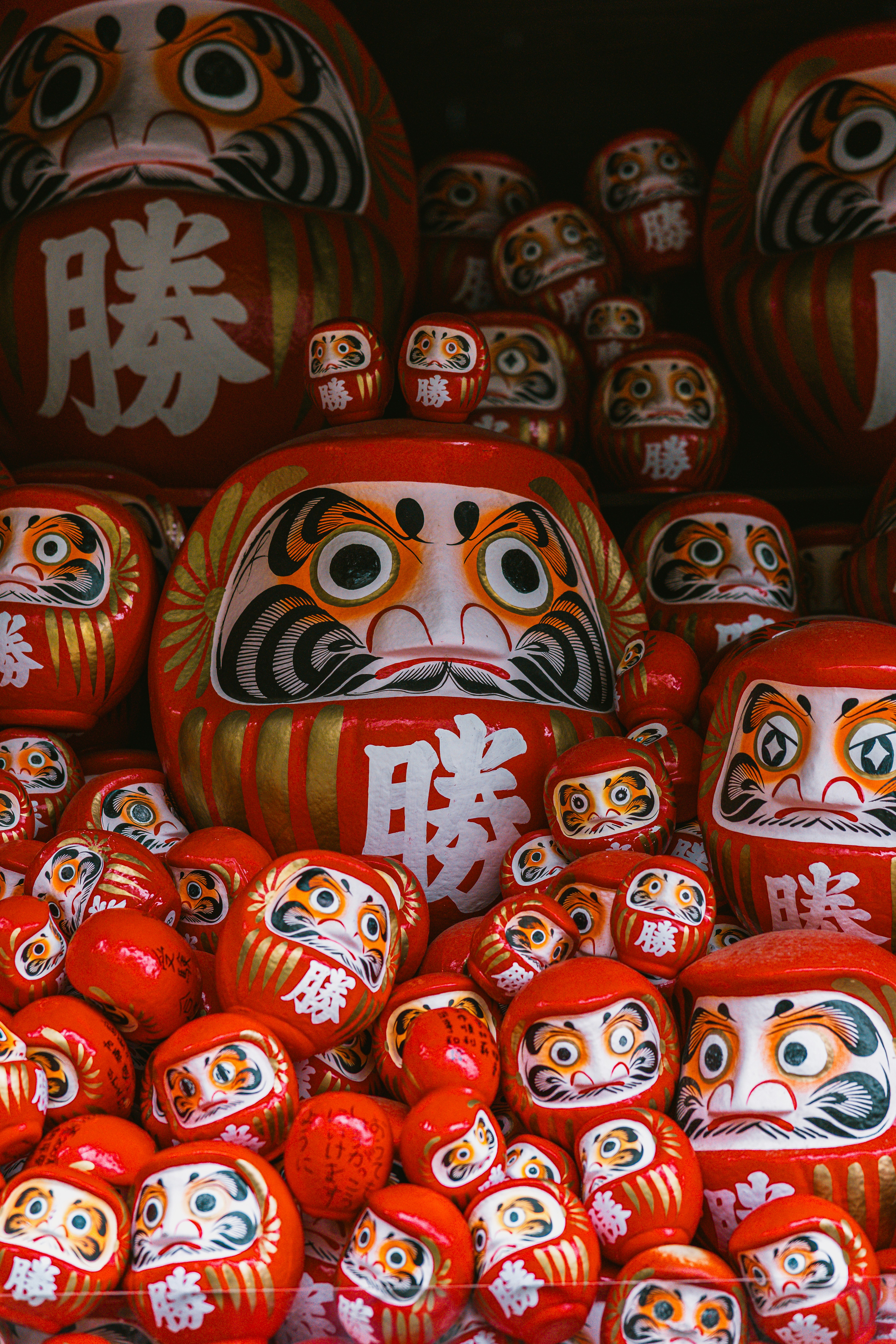 A large collection of red and white Daruma dolls with painted faces