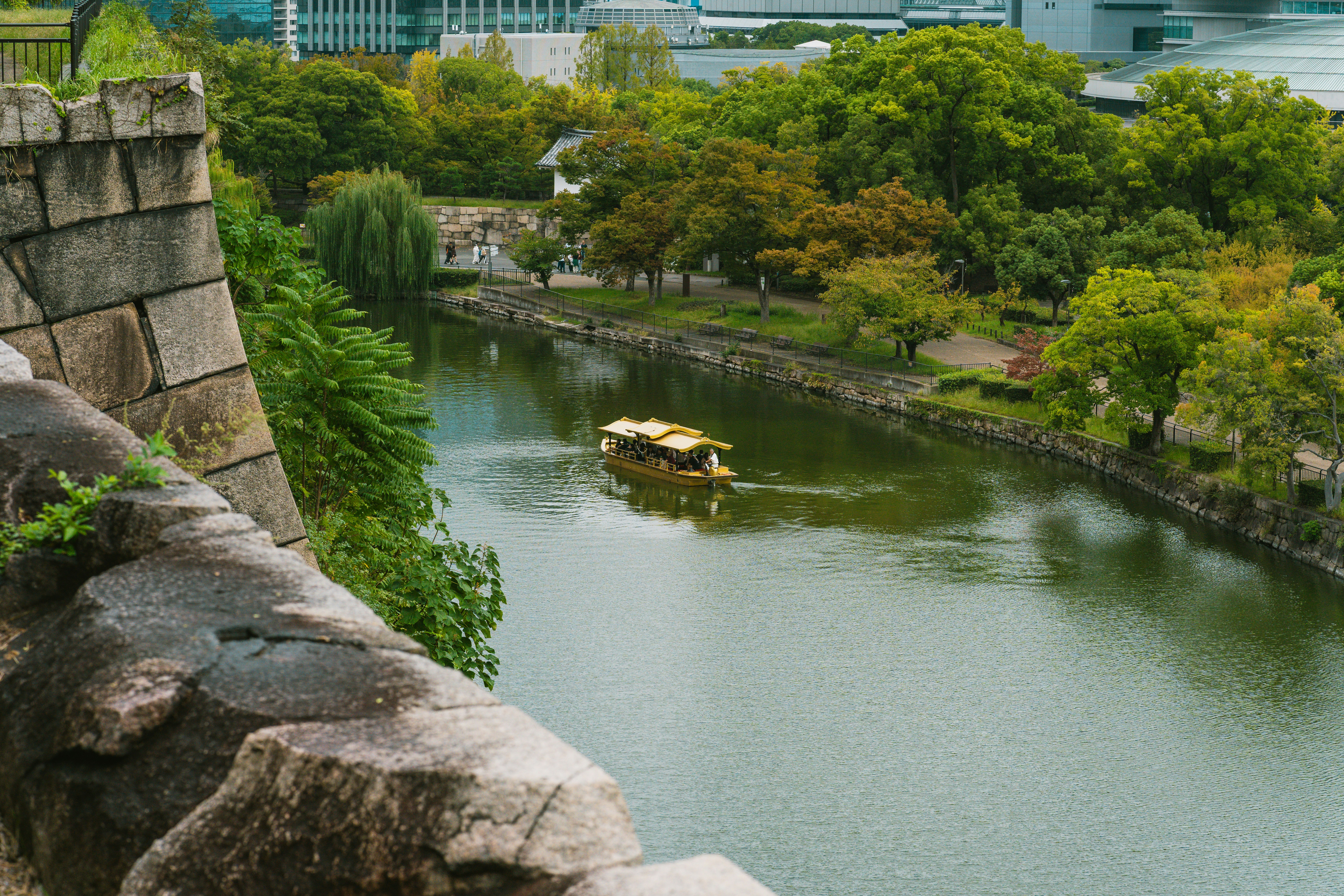 A tour boat on the moat of Osaka Castle surrounded by lush green trees