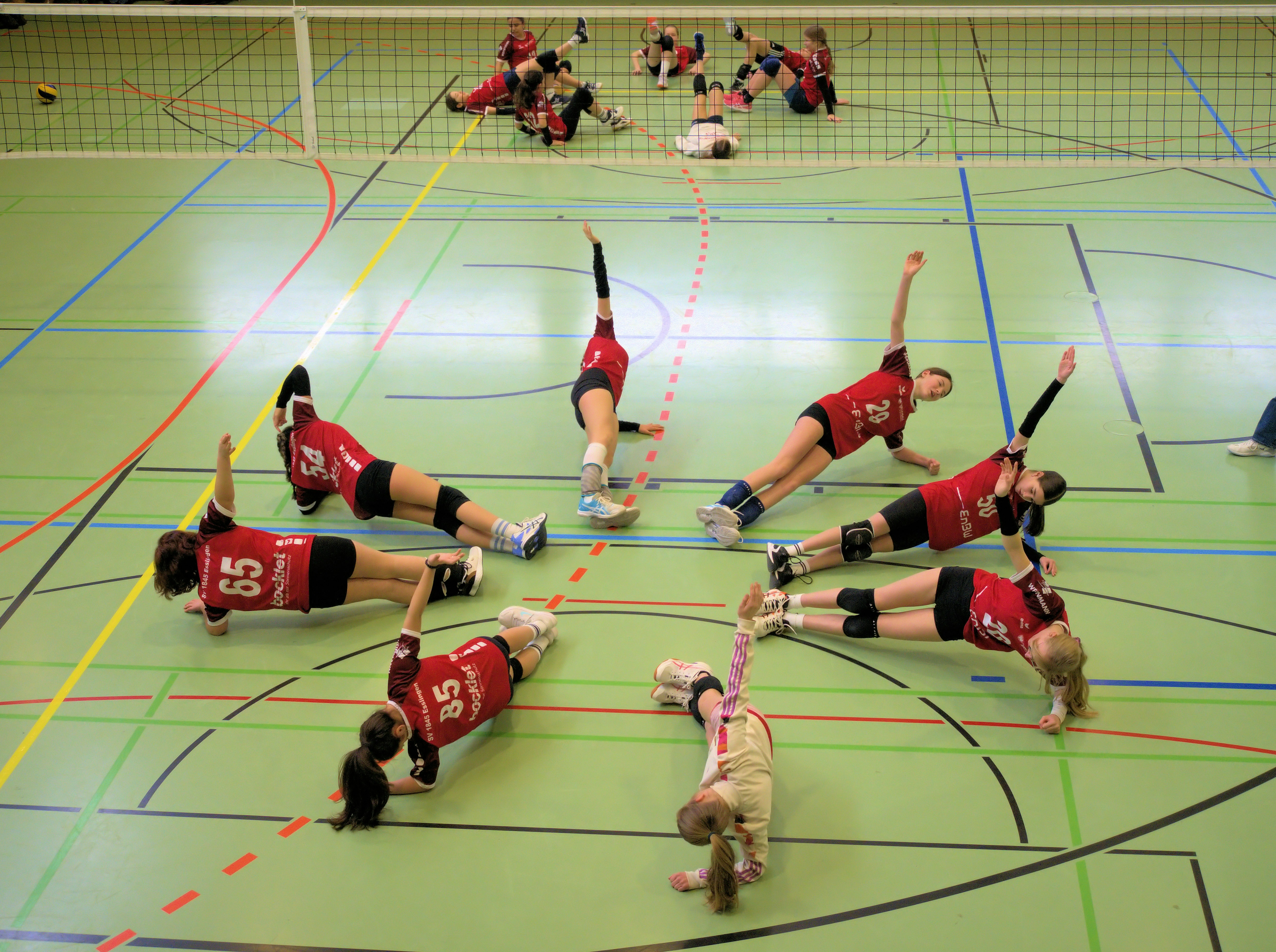 A group of volleyball players in red jerseys performing side planks on a court