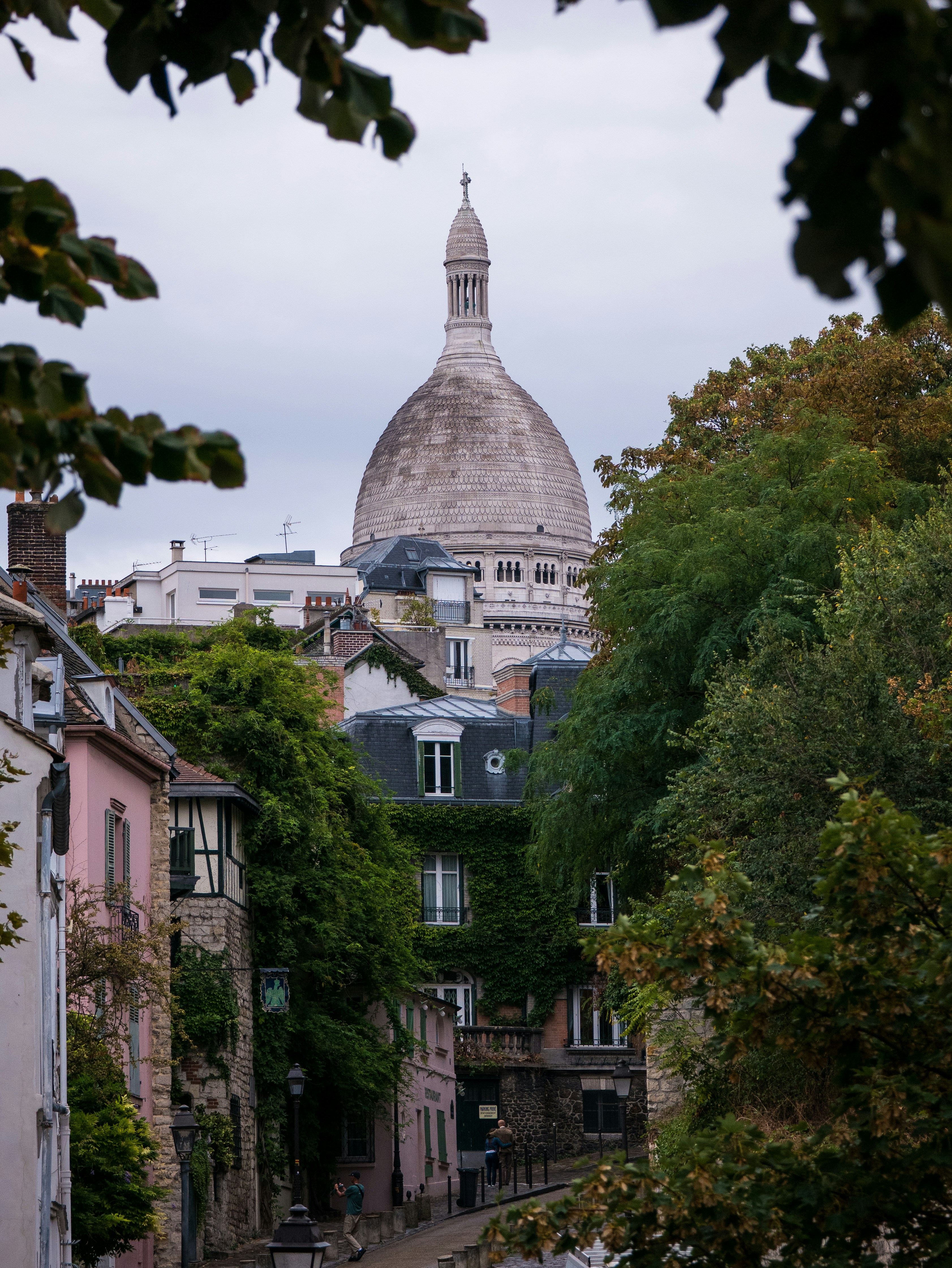 The Sacré-Cœur Basilica dome rising above ivy-covered buildings on a street in Paris