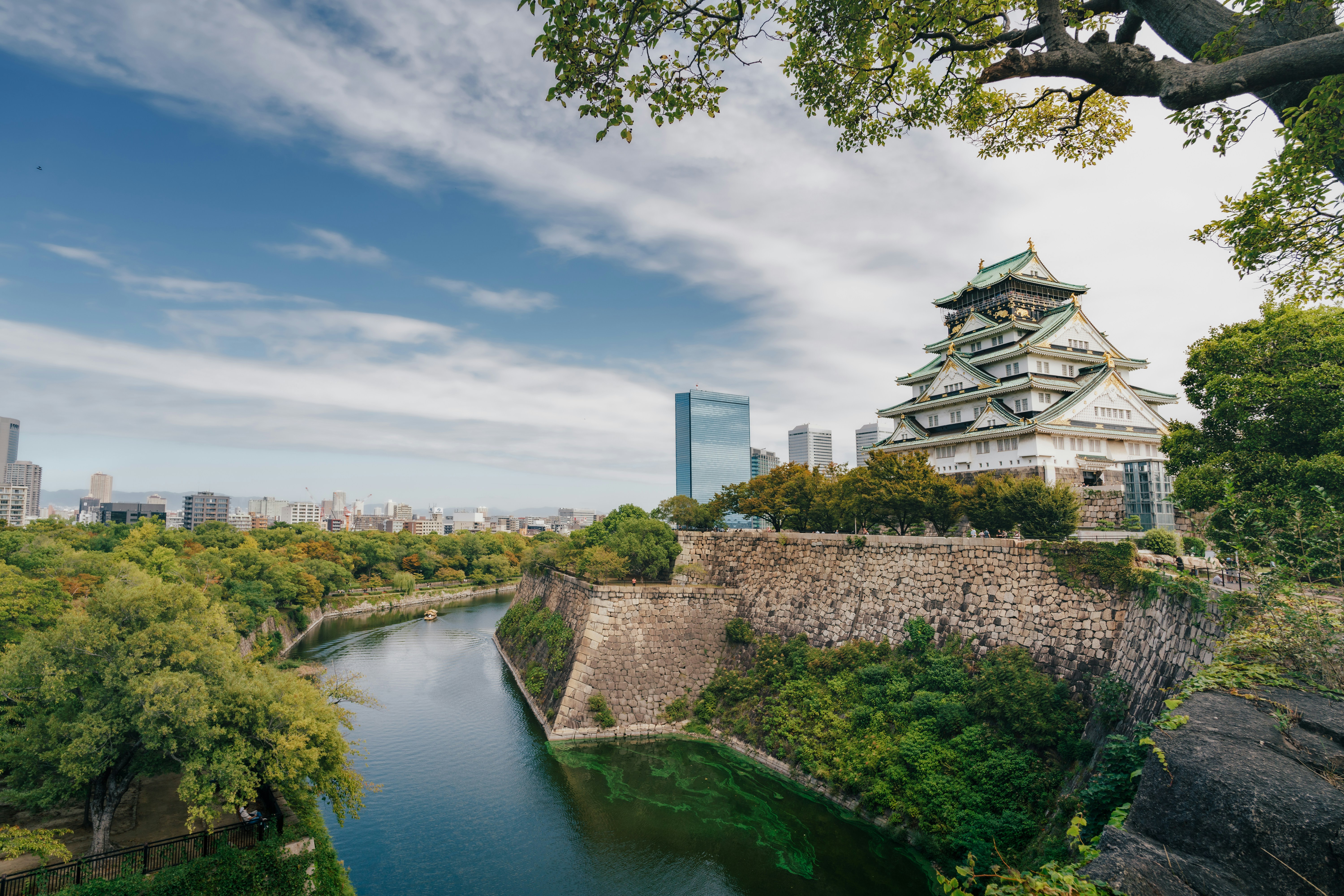 Le château d’Osaka s’élevant au-dessus de murs de pierre et d’un fossé avec une silhouette urbaine
