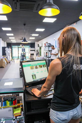 A woman in a black tank top typing on a computer in a shop