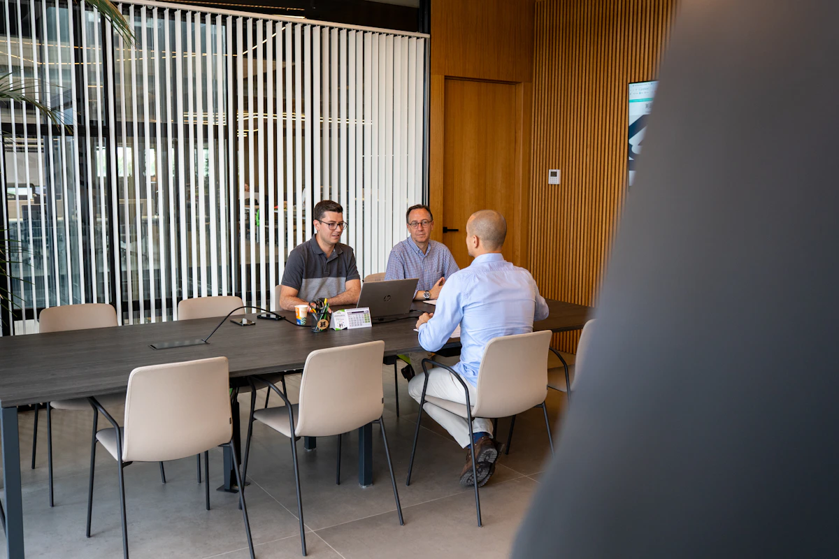 Tiga pria rapat di meja panjang kantor modern