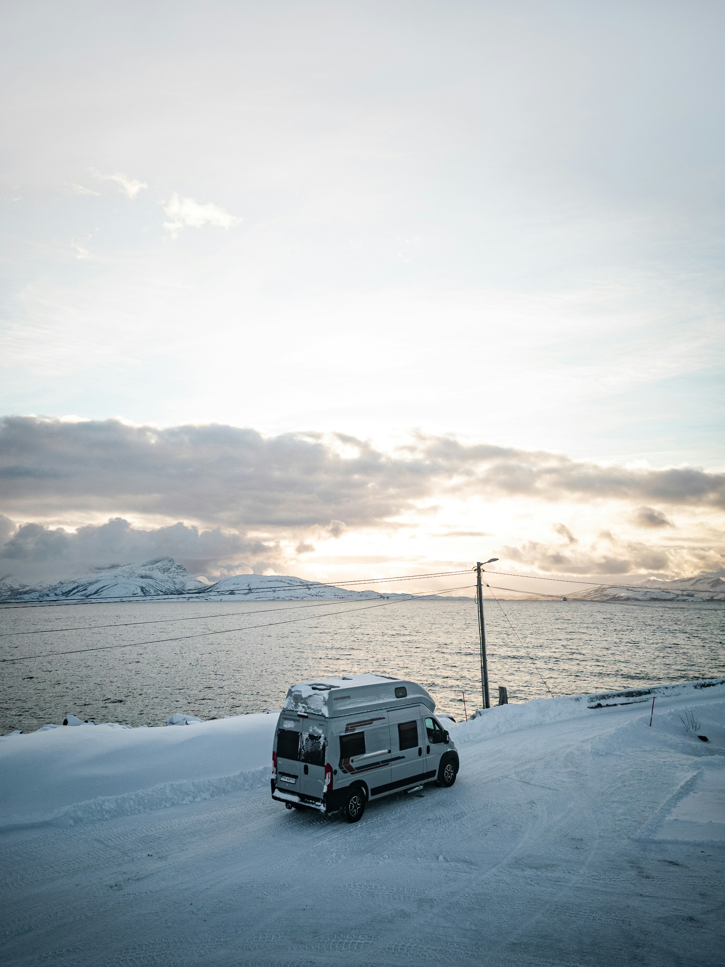 A camper van parked on a snowy road beside a cold sea